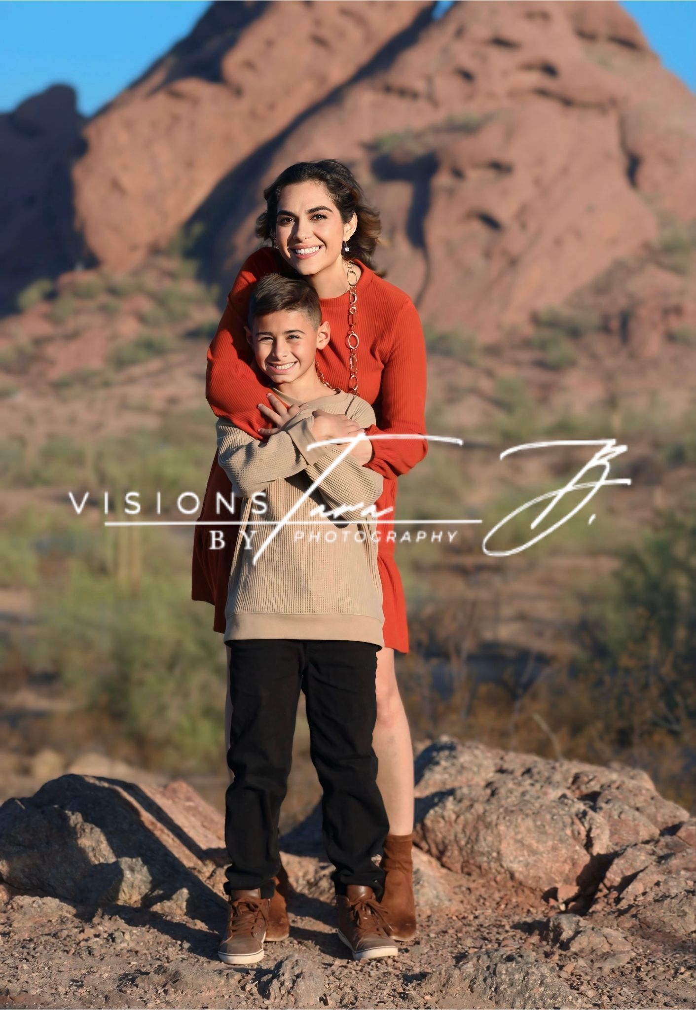 Mom hugging her son in the desert, both smiling as they stand together with mountains and sunlit landscape behind them.