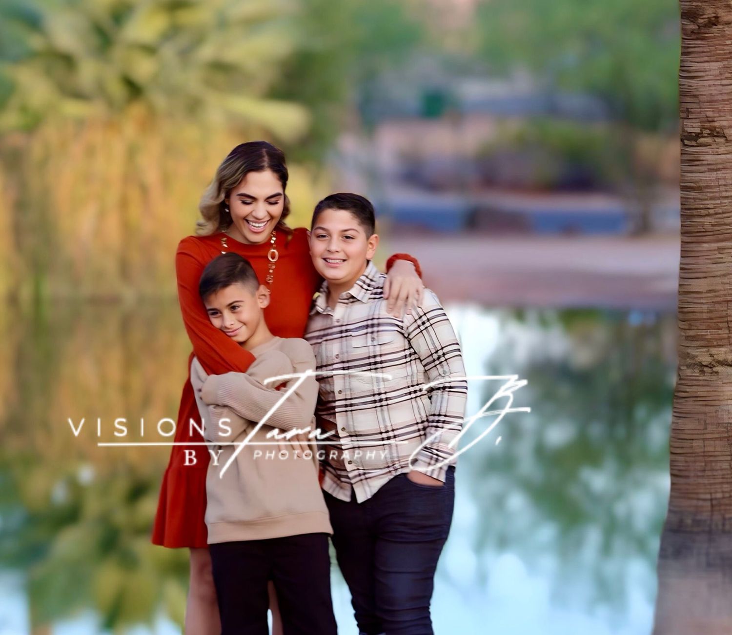 Mom hugging her two sons near a calm lakeside, all smiling warmly in soft afternoon light.