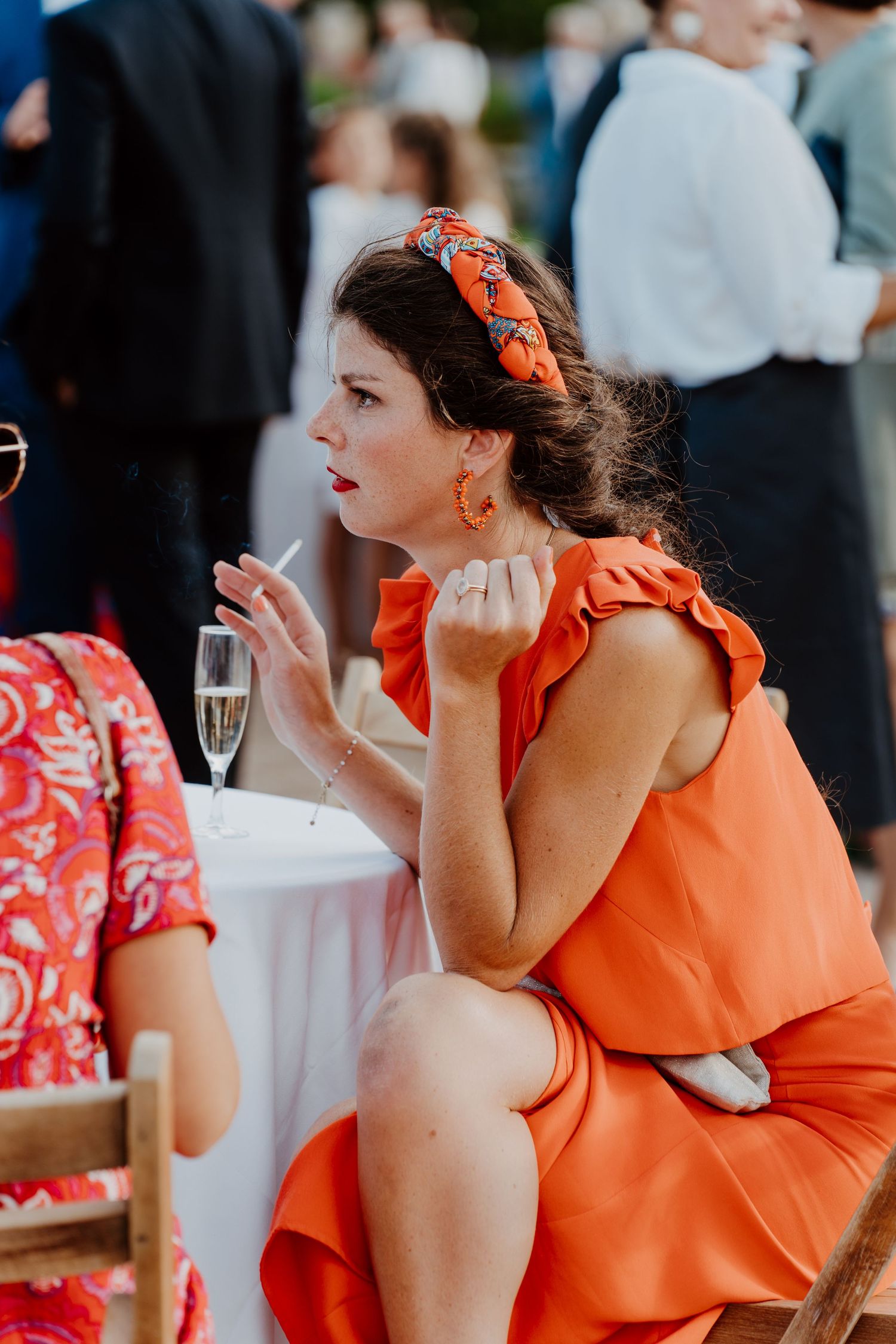 Invitée en robe orange riant à une table haute pendant le cocktail