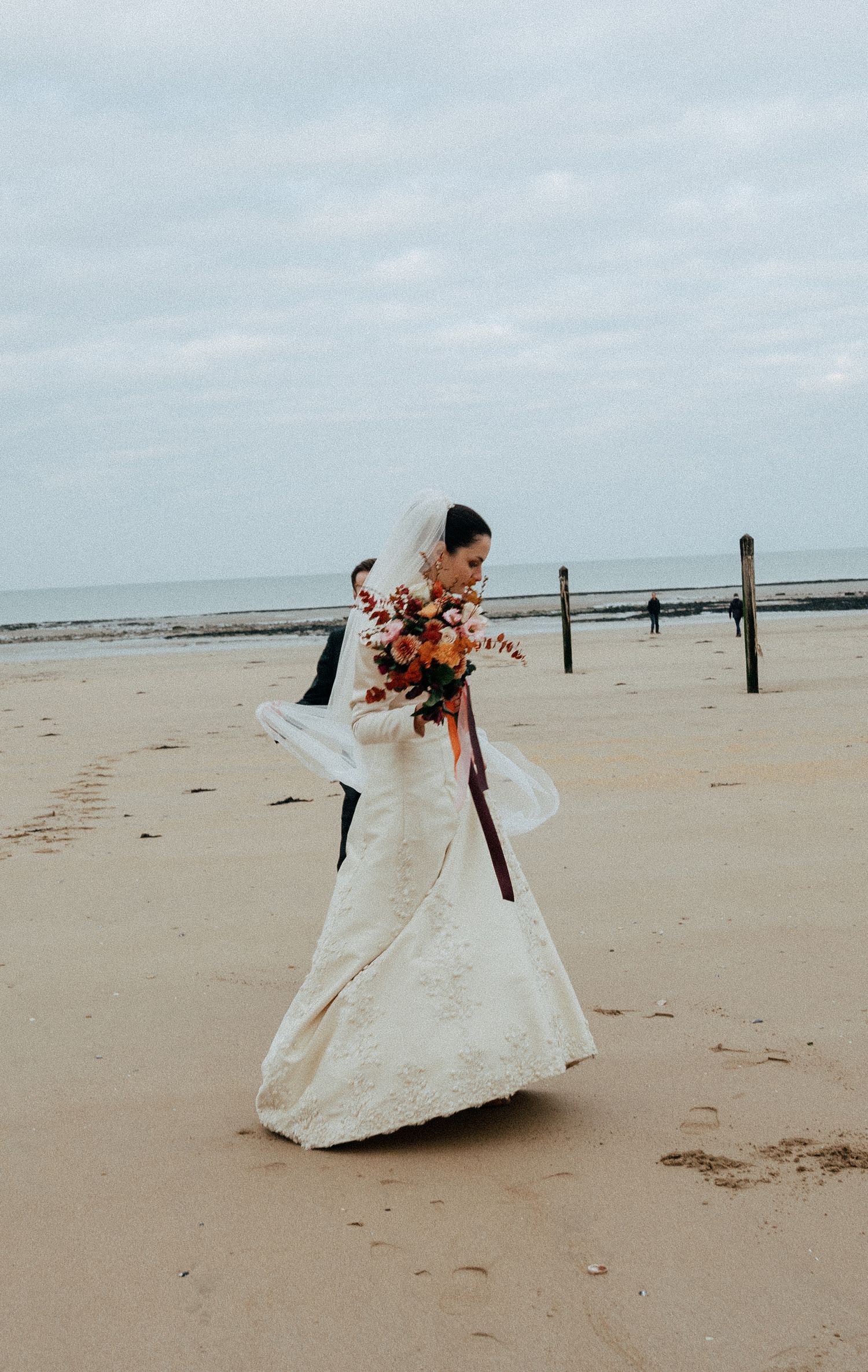 Mariée sur une plage, bouquet à la main, robe au vent Mariage d'hiver