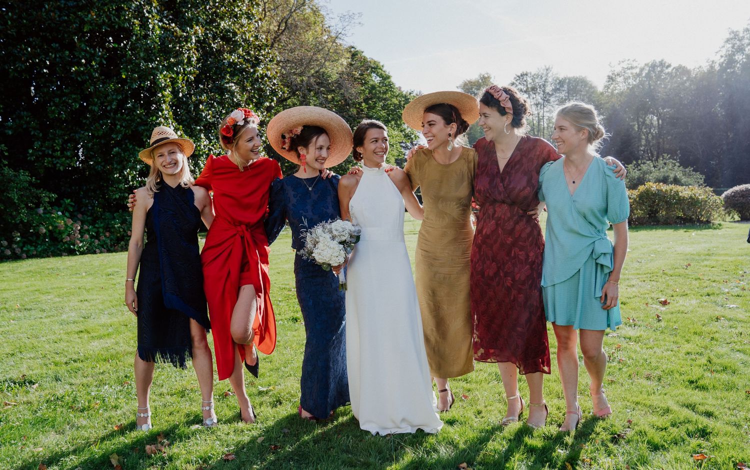 Mariée entourée de son groupe d'amies en robes colorées sur la pelouse