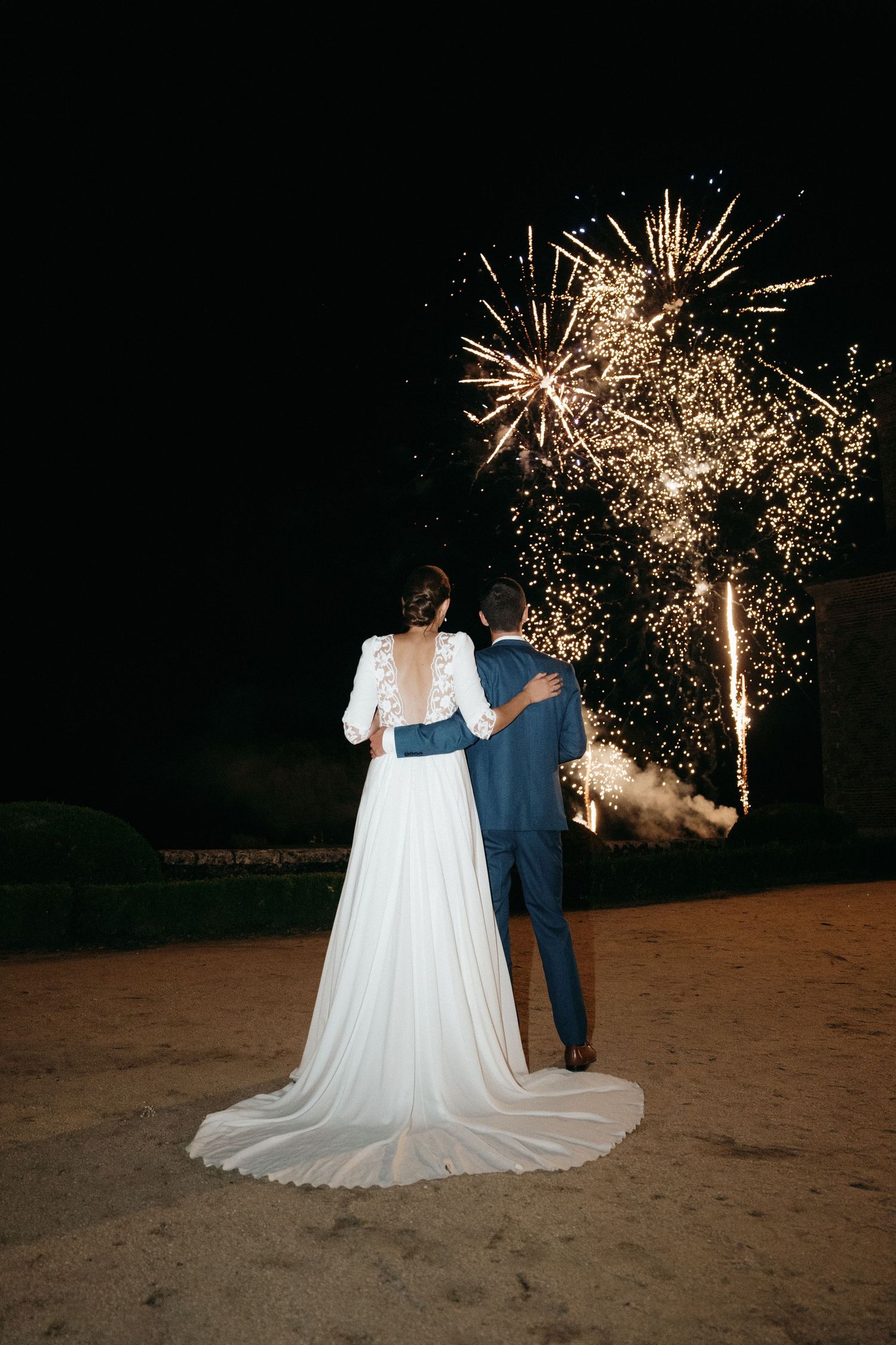Newlywed couple embraces while watching a stunning fireworks display light up the night sky.