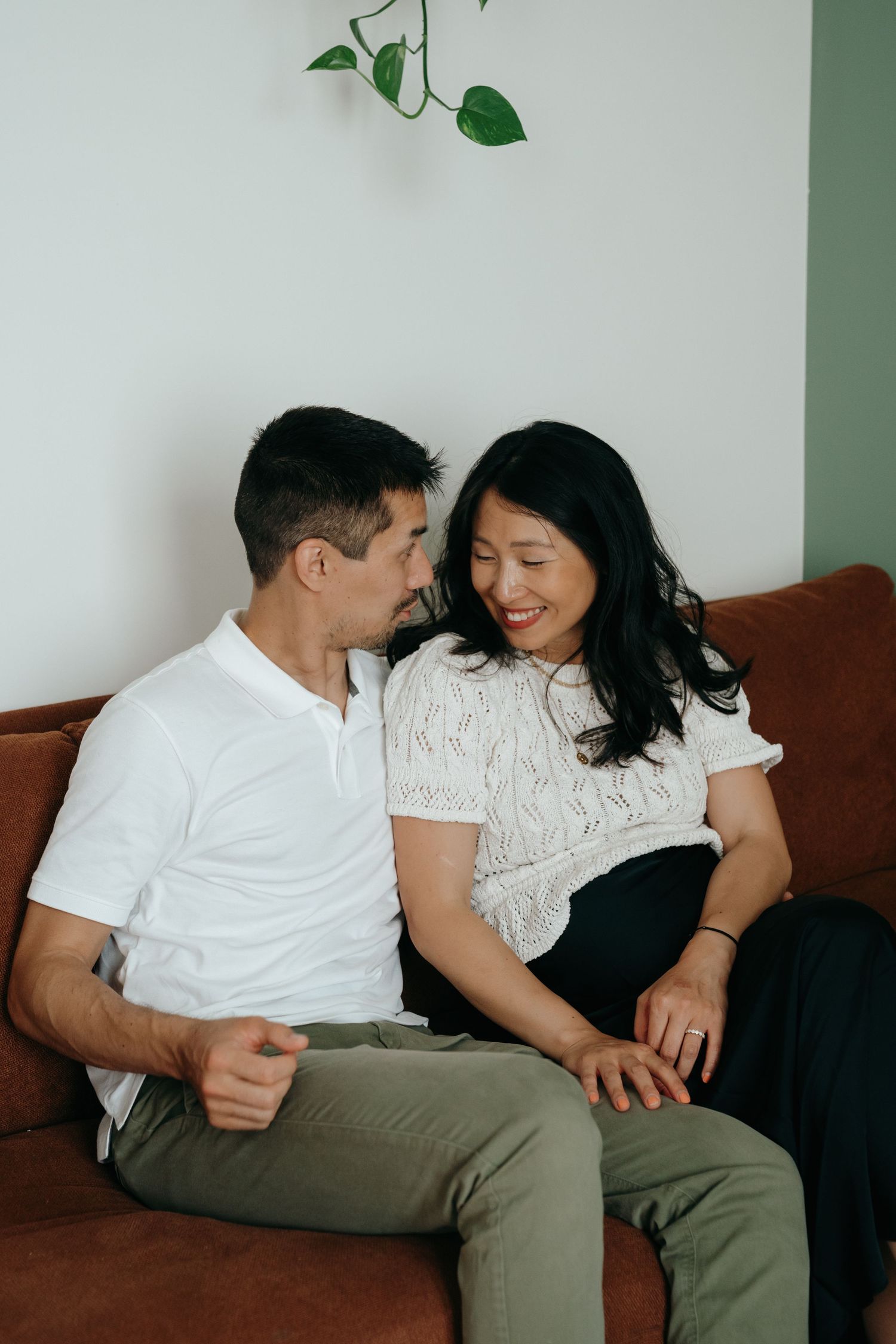 Happy couple sits closely together on a brown sofa, sharing an intimate moment at home.