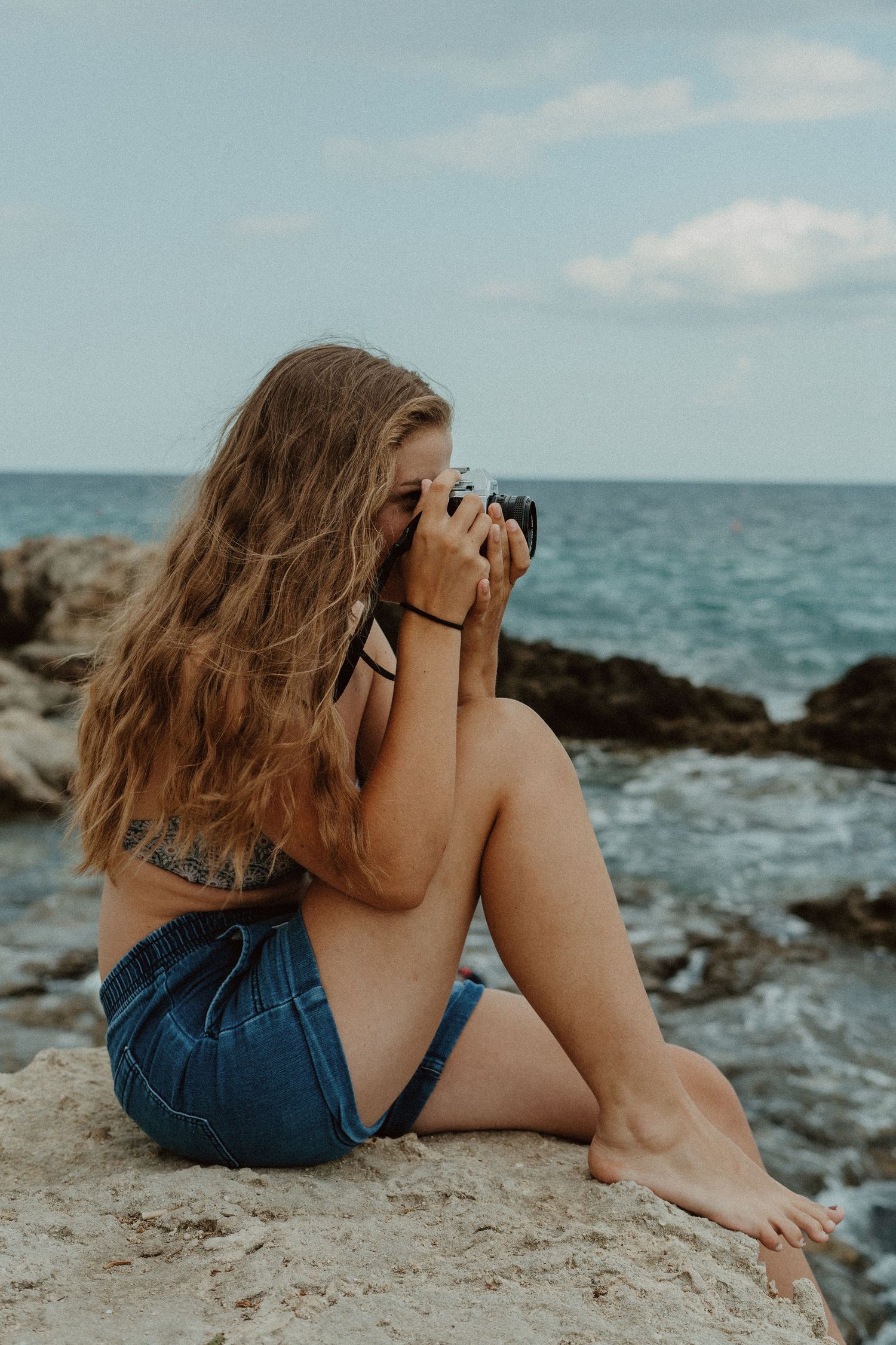 Femme photographiant assise sur des rochers en bord de mer