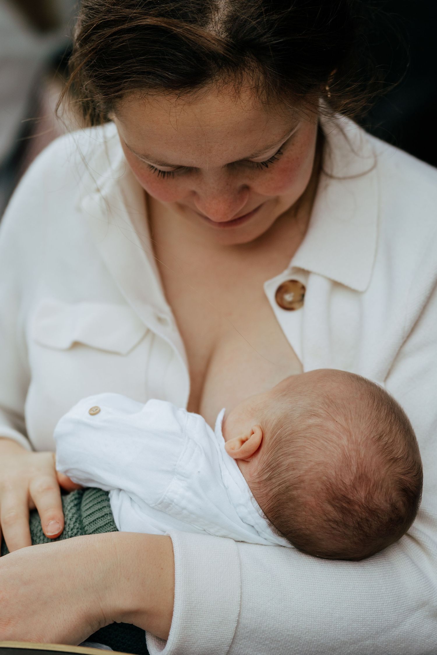 A mother tenderly breastfeeding her newborn baby while wearing a white linen shirt.