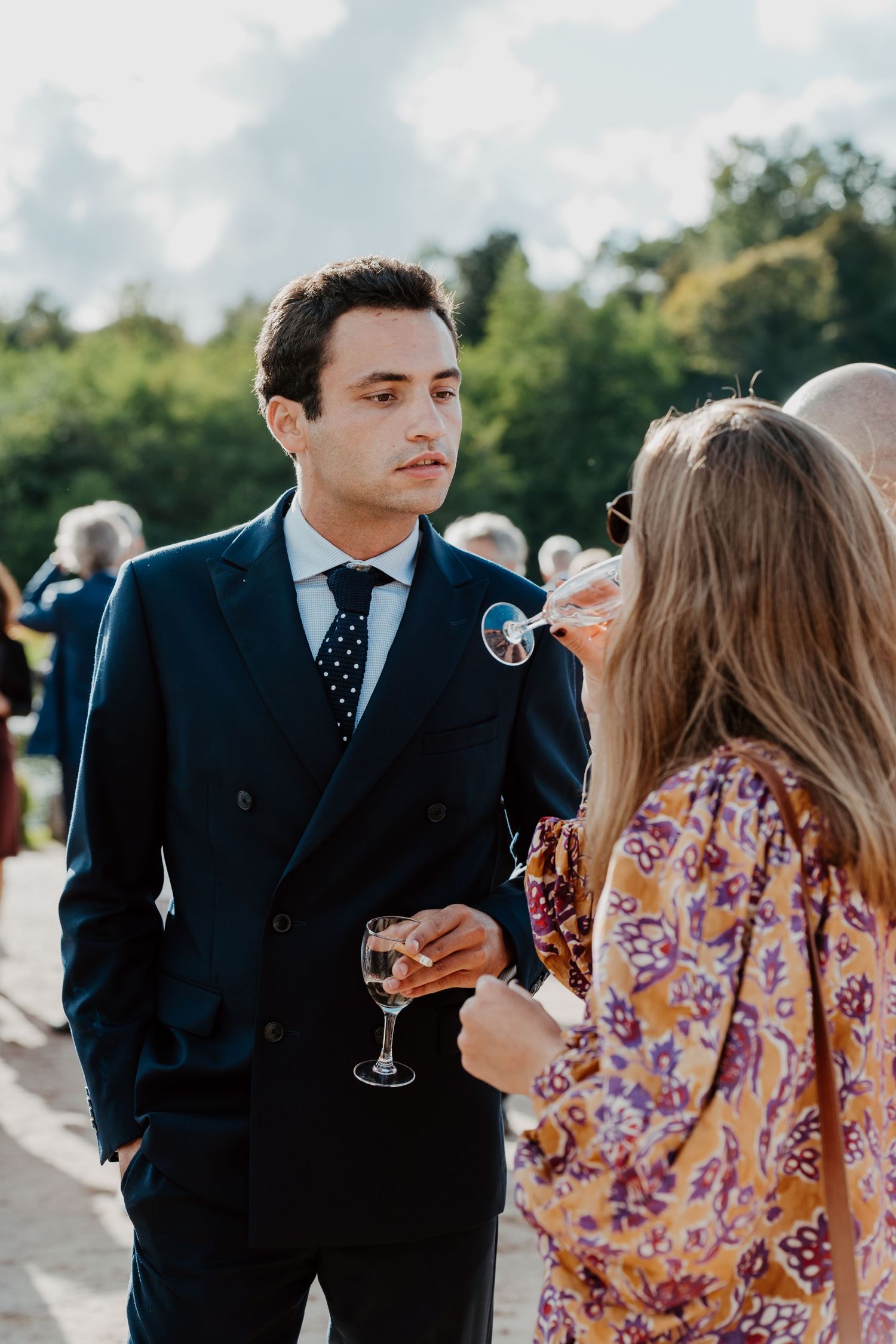 Invité en costume et invitée en robe fleurie partageant un moment complice pendant le cocktail