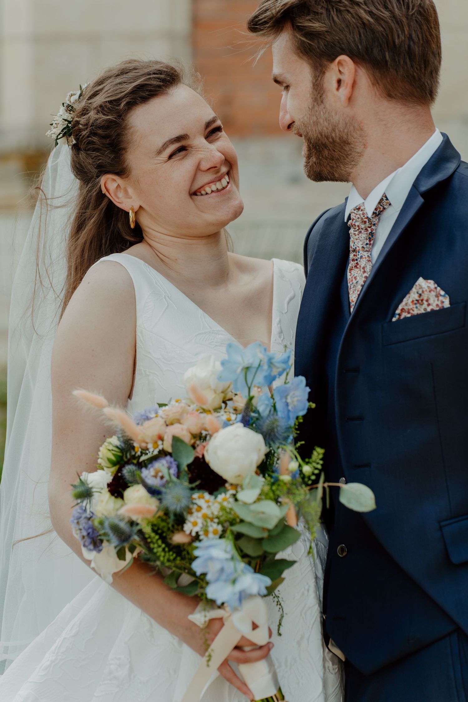Mariée souriante tenant un bouquet bleu et blanc, marié à ses côtés