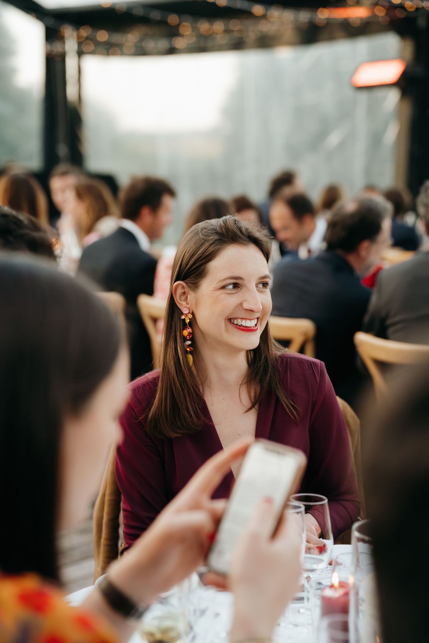 Joyful woman with statement earrings and red lips smiling at a candlelit wedding reception dinner.