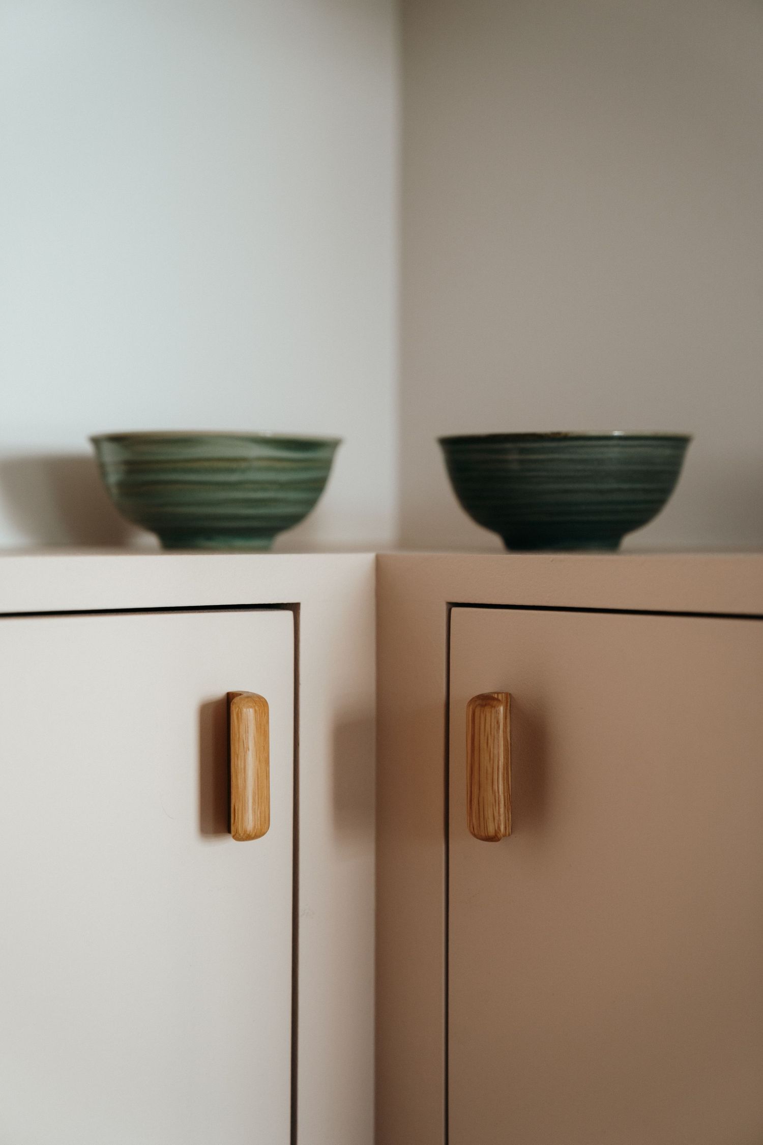 Two green ceramic bowls on top of white cabinets with wooden handles in a minimalist interior.