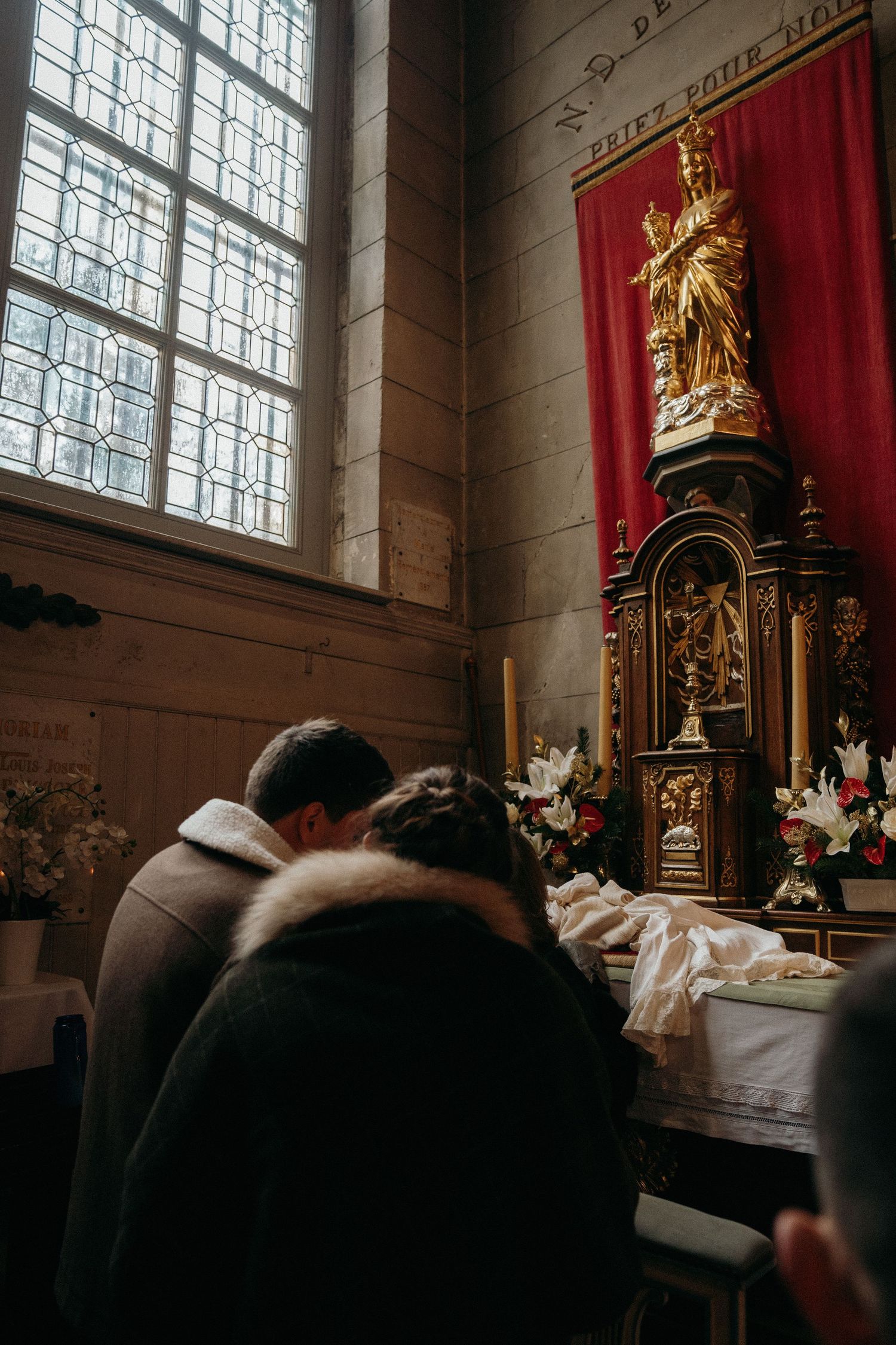 Couple praying together before ornate golden saint statue in historic stone church interior.