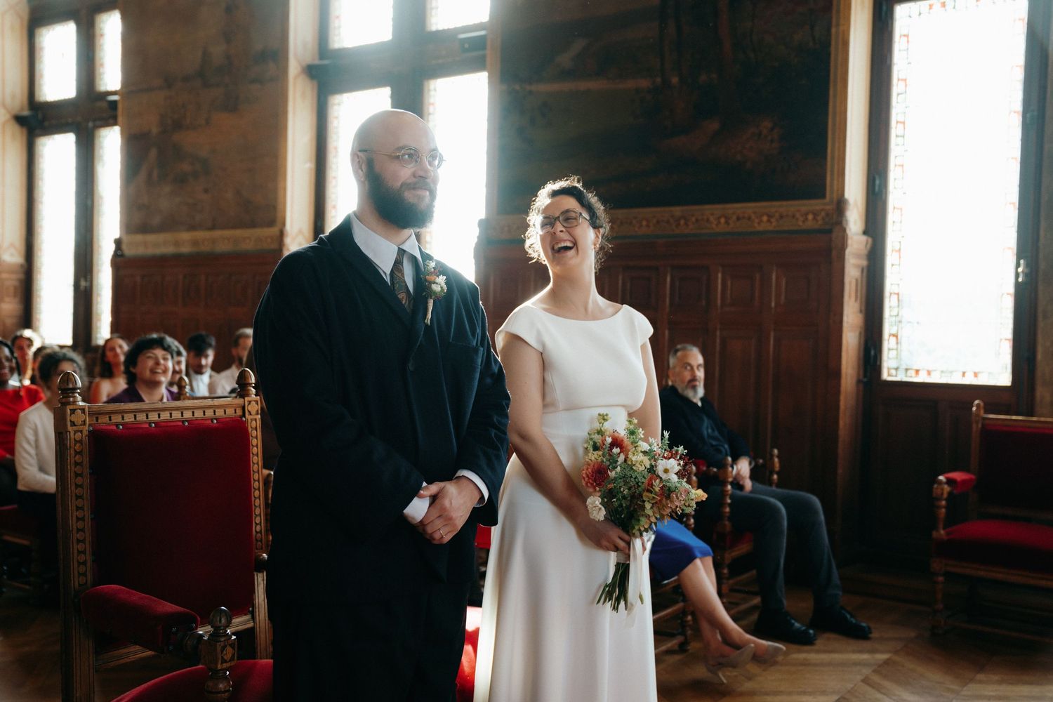 Bride laughing joyfully during civil wedding ceremony in elegant historic hall with wooden decor.