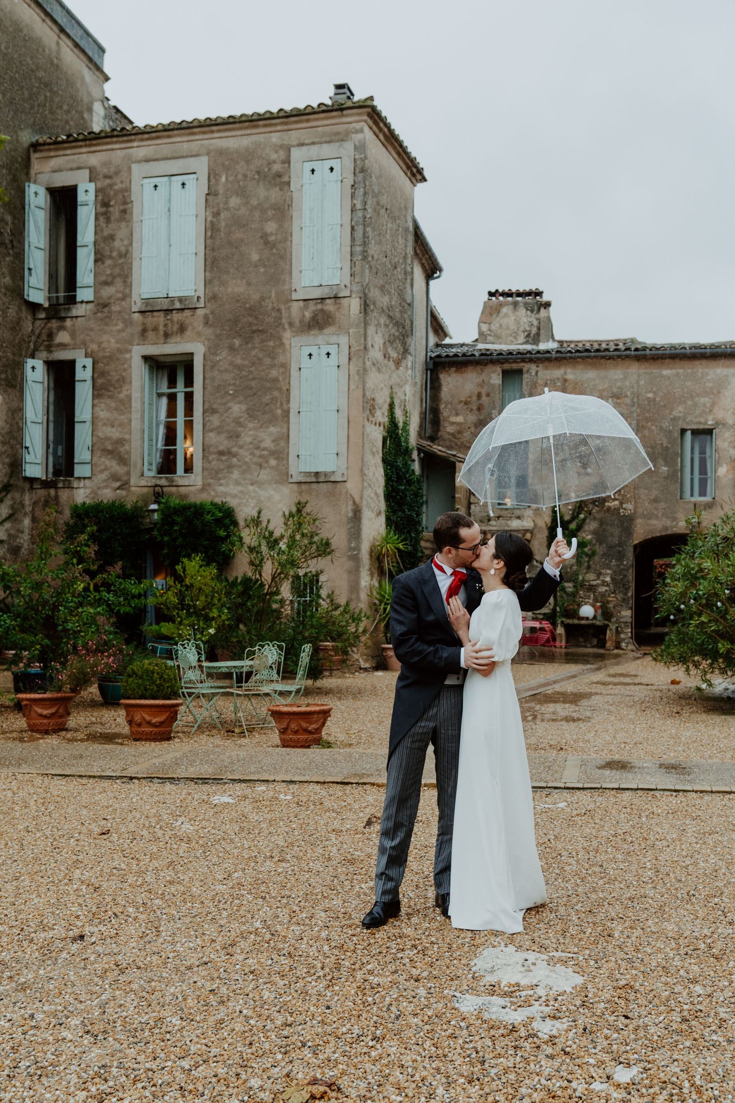 Mariés sous un parapluie devant une bâtisse en pierre, mariage près de Montpellier