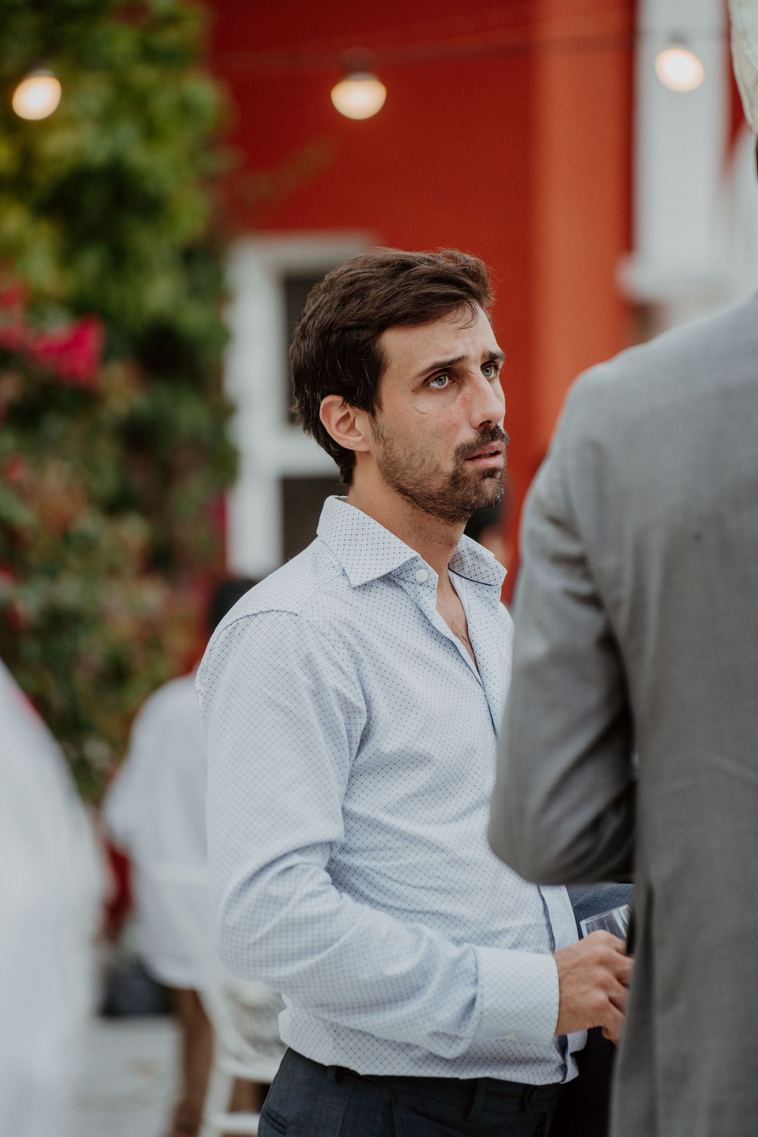 Invité en chemise blanche discutant devant une façade rouge pendant le cocktail