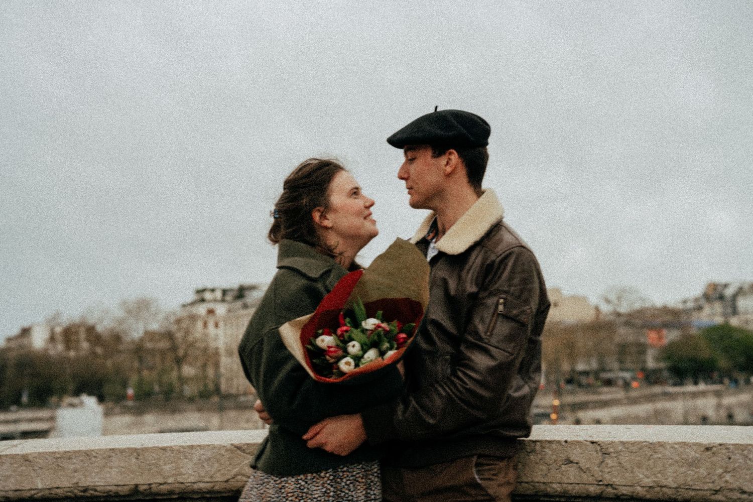 Couple sharing a romantic moment with red flower bouquet by Paris riverside.