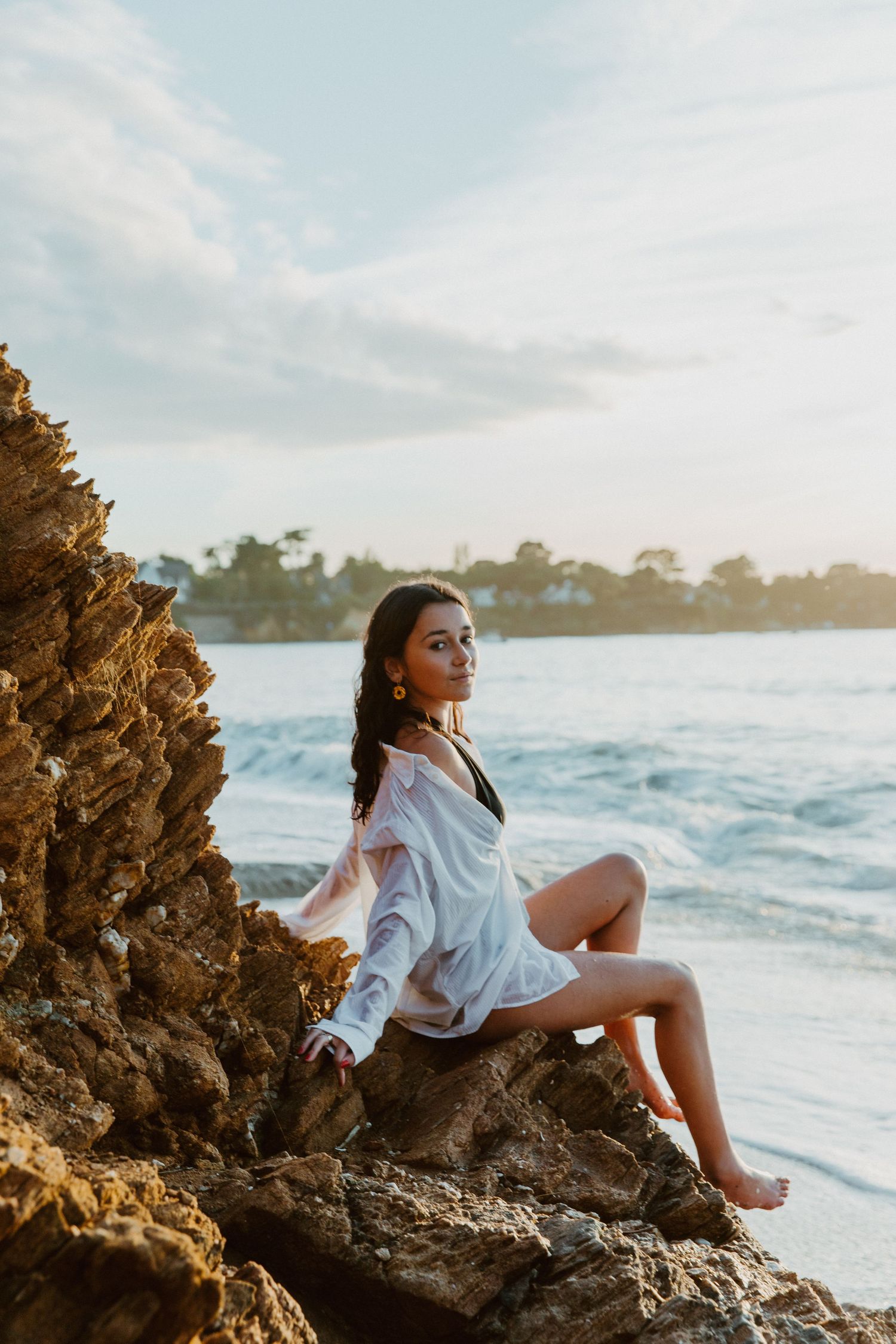 Femme assise sur des rochers face à la mer