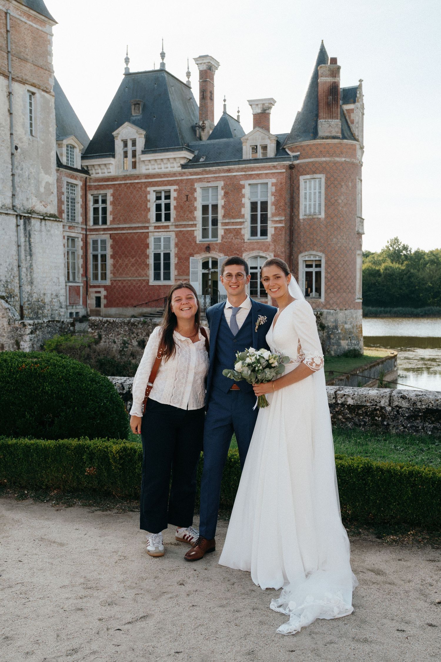 Mariés posant avec leur photographe devant un château