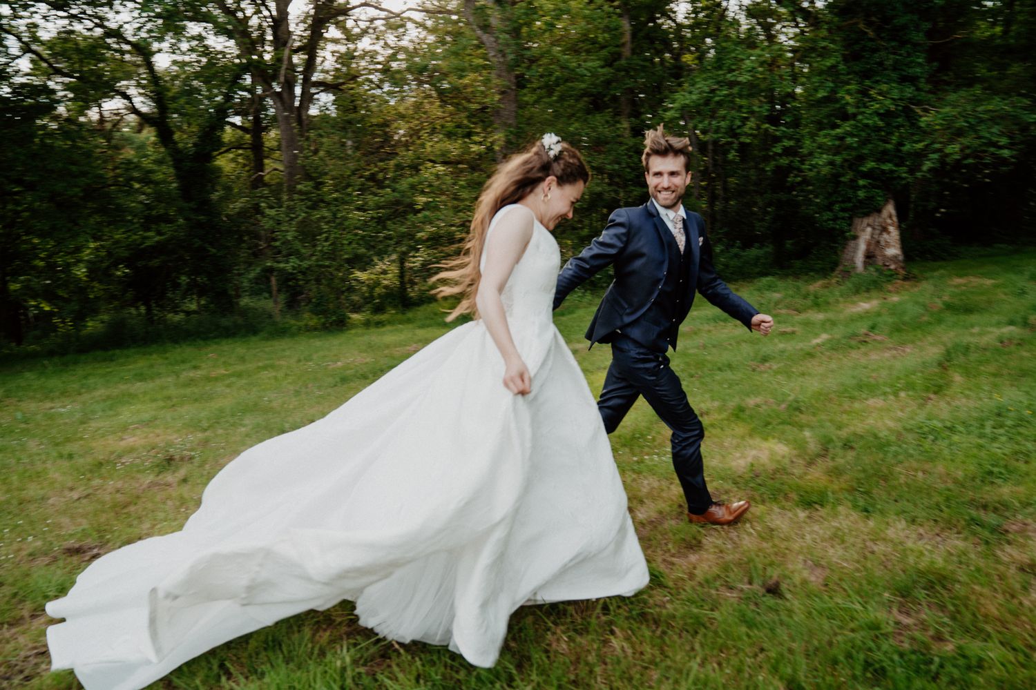 Mariés courant en riant dans un champ, robe de mariée virevoltante
