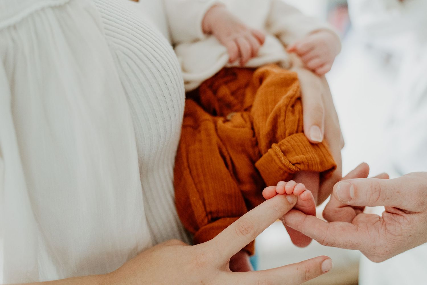 Close-up of an adult gently holding a newborn baby's tiny feet wrapped in orange muslin cloth.