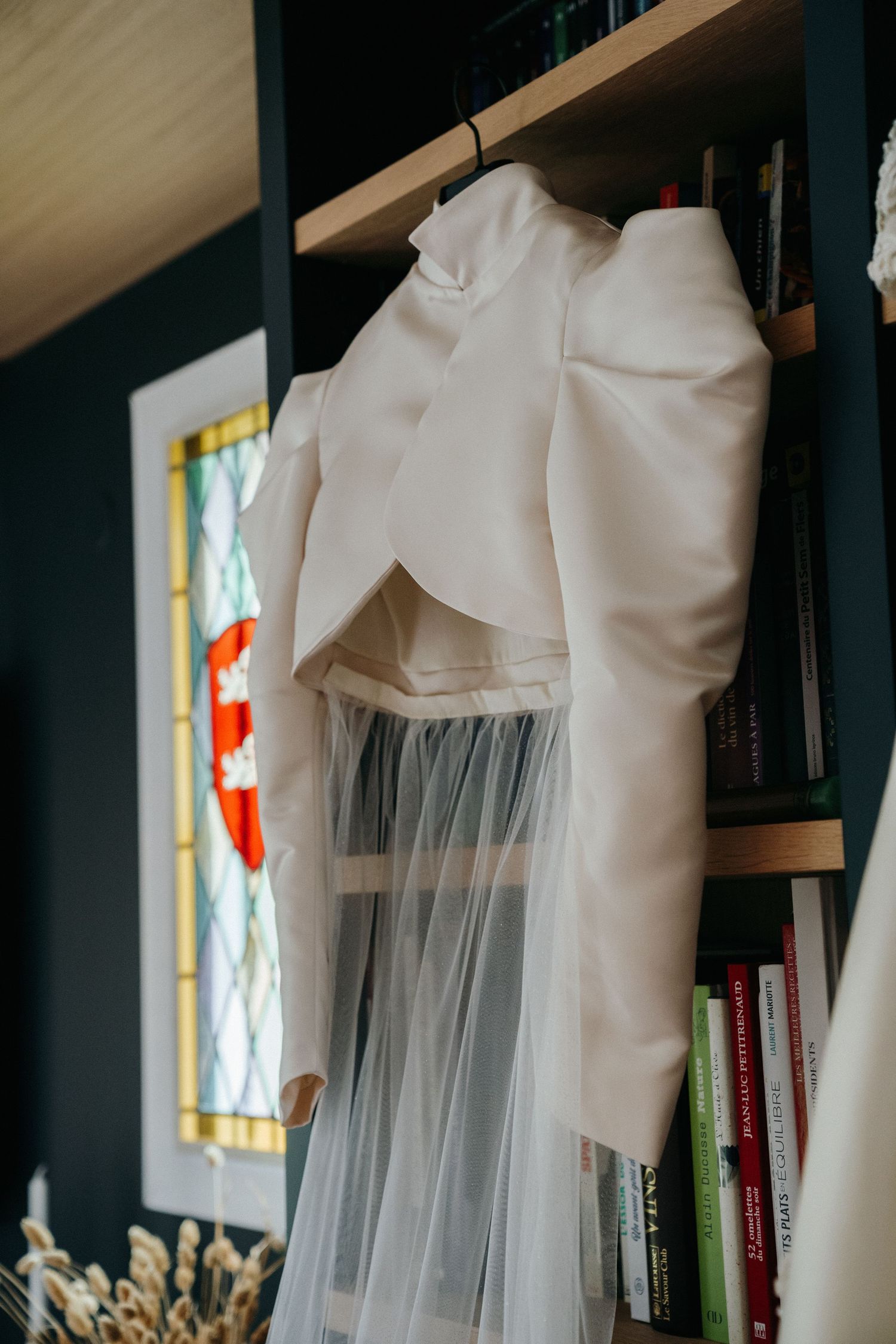 Robe de mariée et voile suspendus devant une bibliothèque, préparatifs de la mariée
