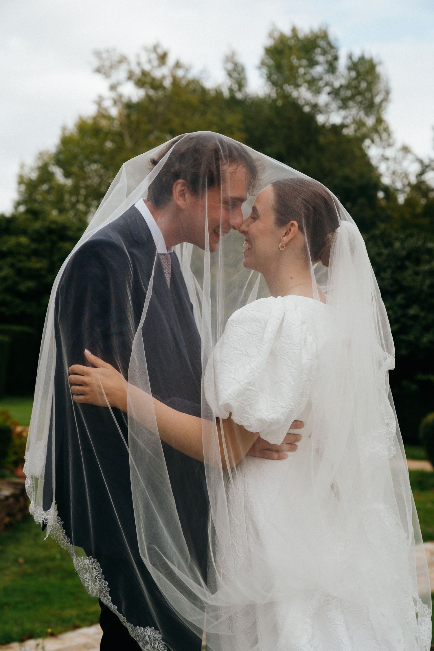 Bride and groom sharing romantic moment under flowing white veil in lush garden setting.