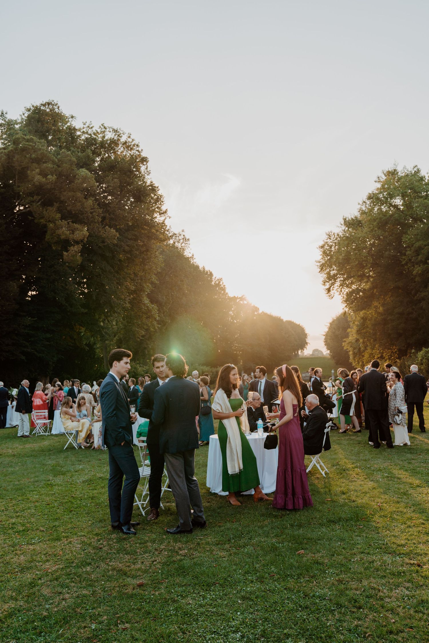Invités de mariage réunis sur la pelouse au coucher du soleil pendant le cocktail