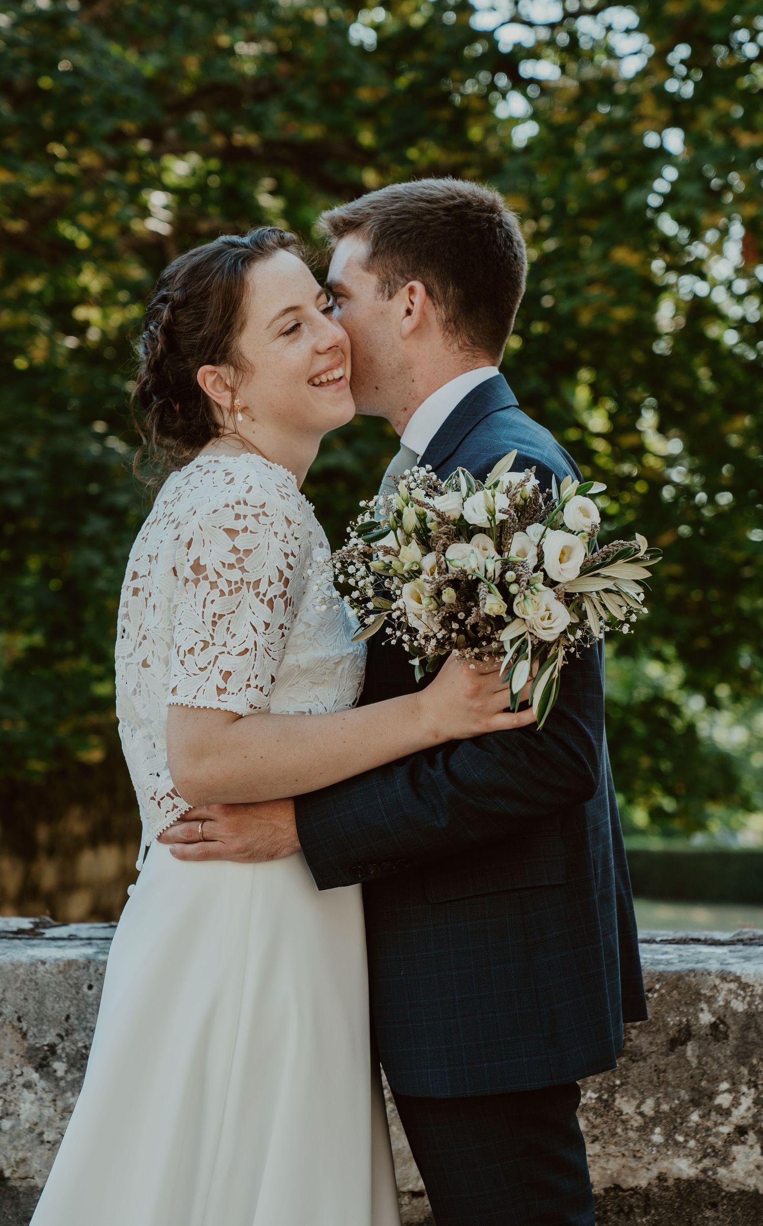 Mariés enlacés, mariée en dentelle tenant un bouquet