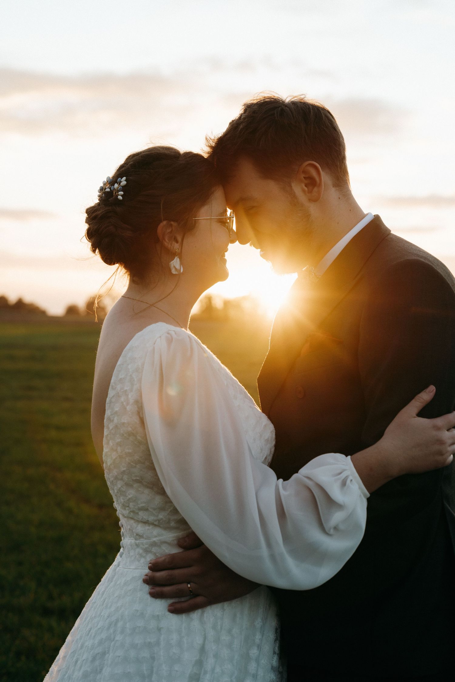 Bride and groom touching foreheads romantically with golden sunset glowing behind them.