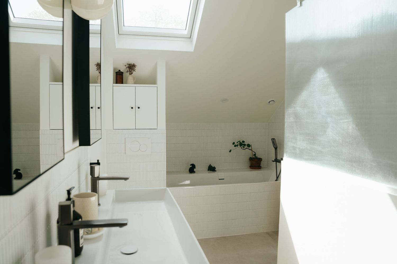 Bright white bathroom with skylight, double sink, built-in bathtub, and small potted plants.