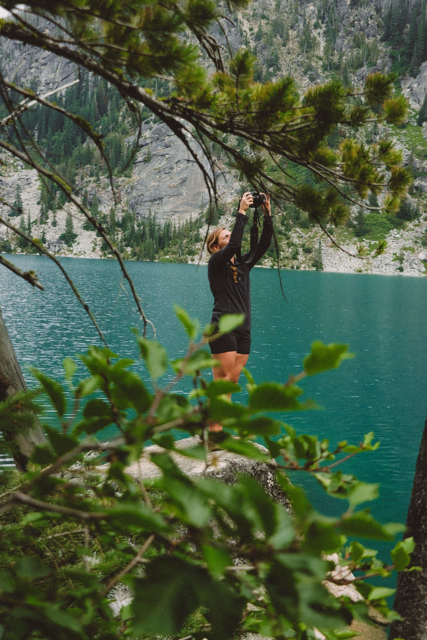 Vibrant turquoise alpine lake framed by pine branches and steep mountain cliffs.
