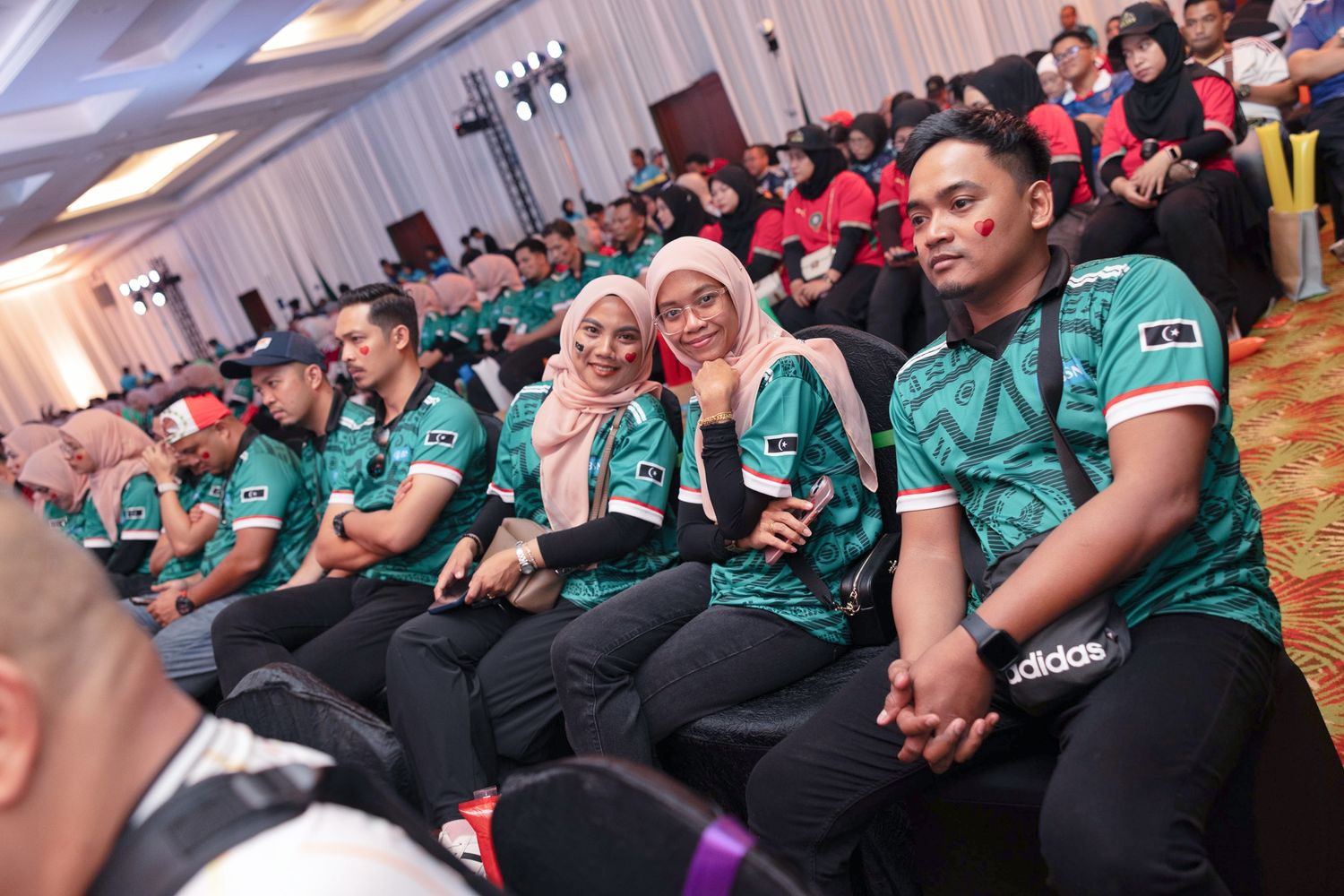 Corporate team members in teal Adidas jerseys seated at a formal BSN company event.