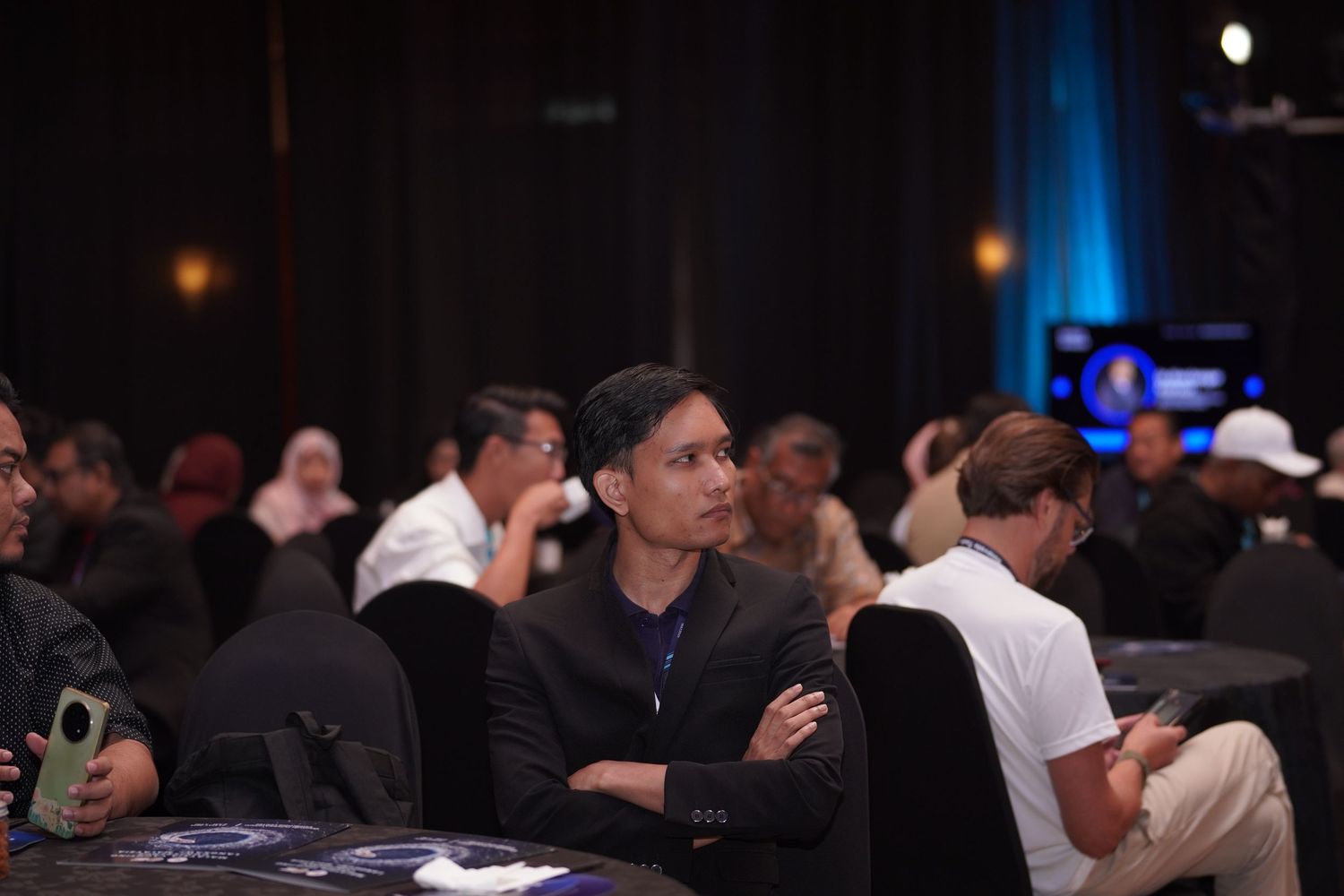 Conference attendees seated in dark auditorium during presentation.