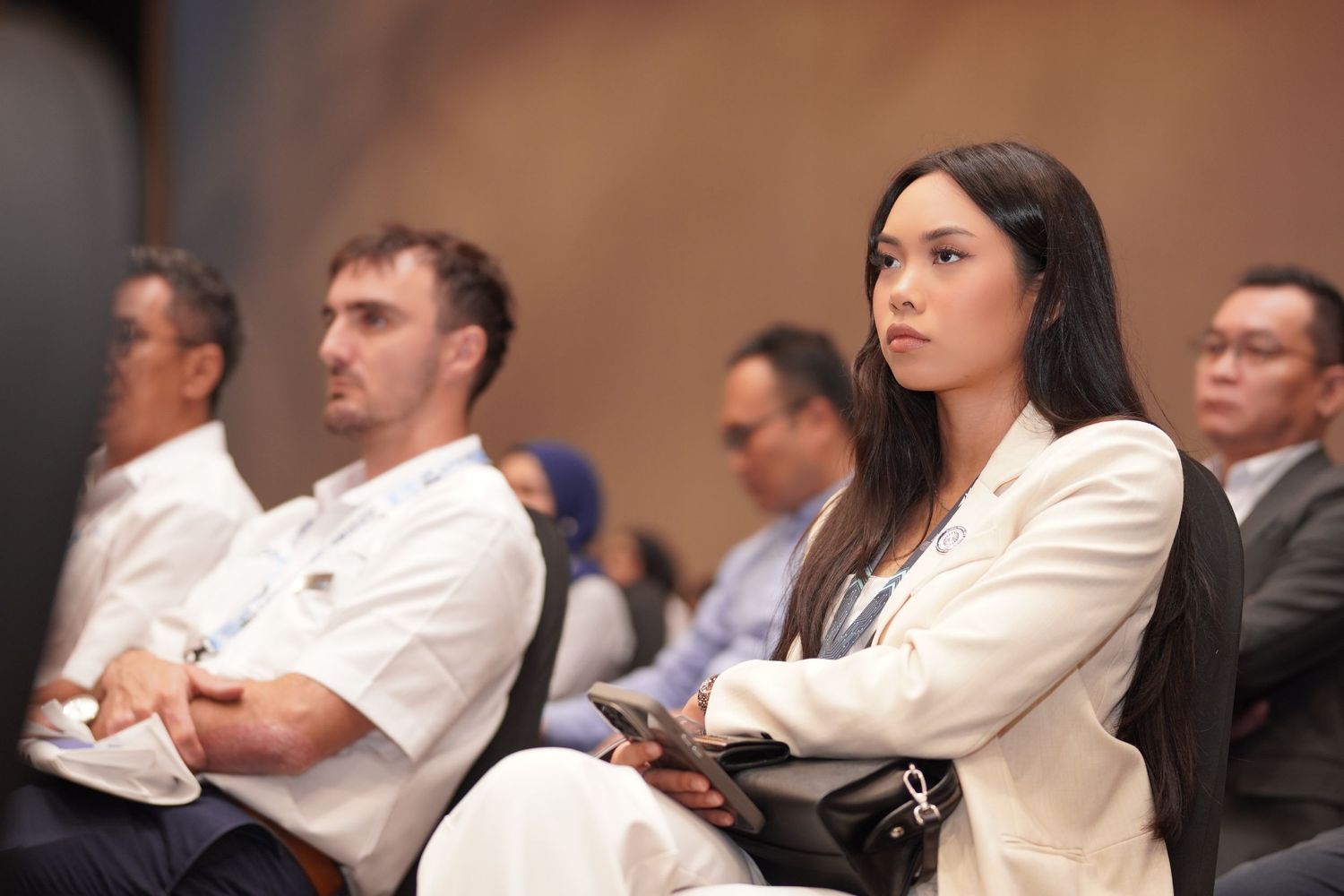 Diverse audience members watch intently during a professional conference presentation.