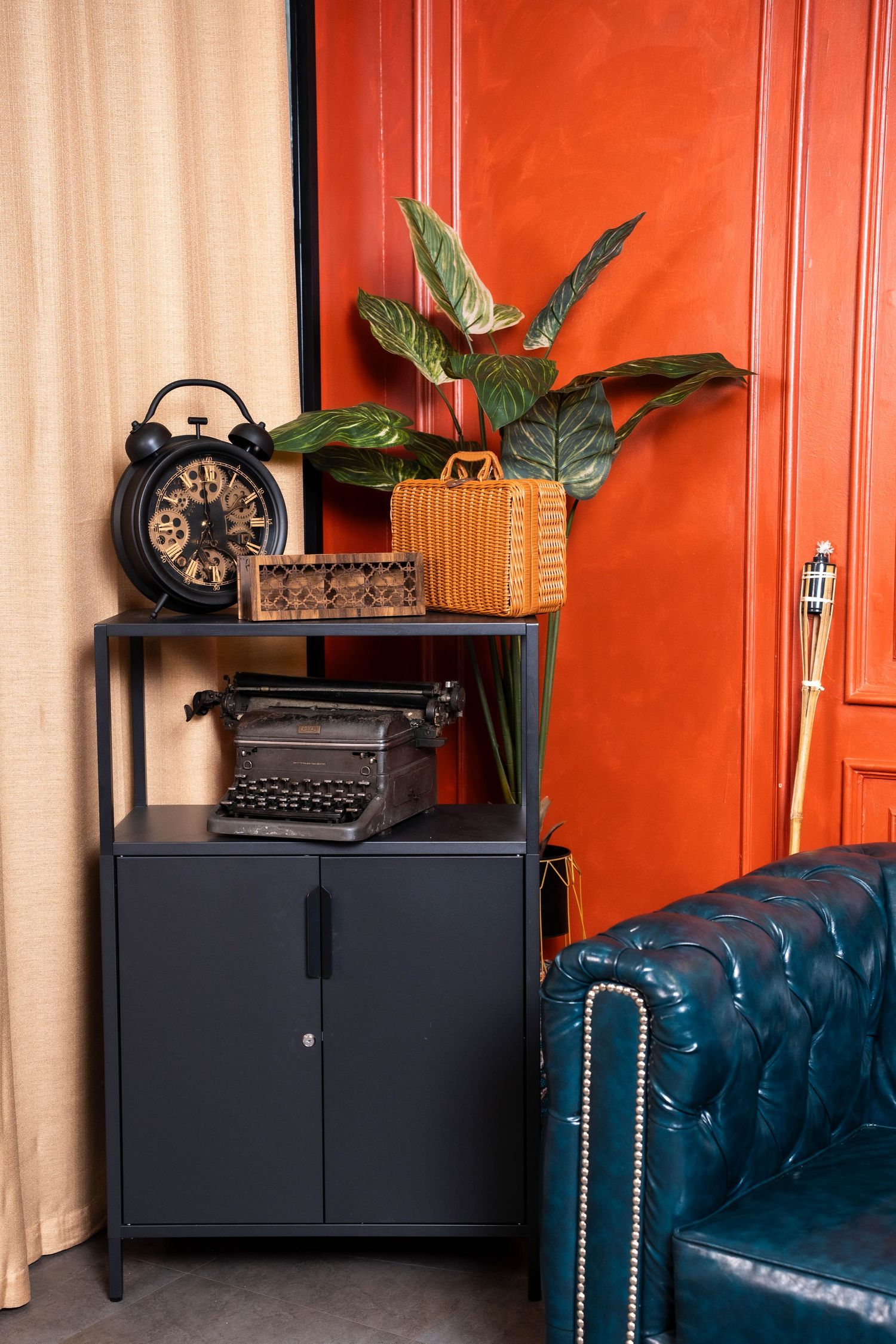 Vintage decor setup with orange walls featuring antique typewriters, black cabinets, and a tufted blue velvet sofa.