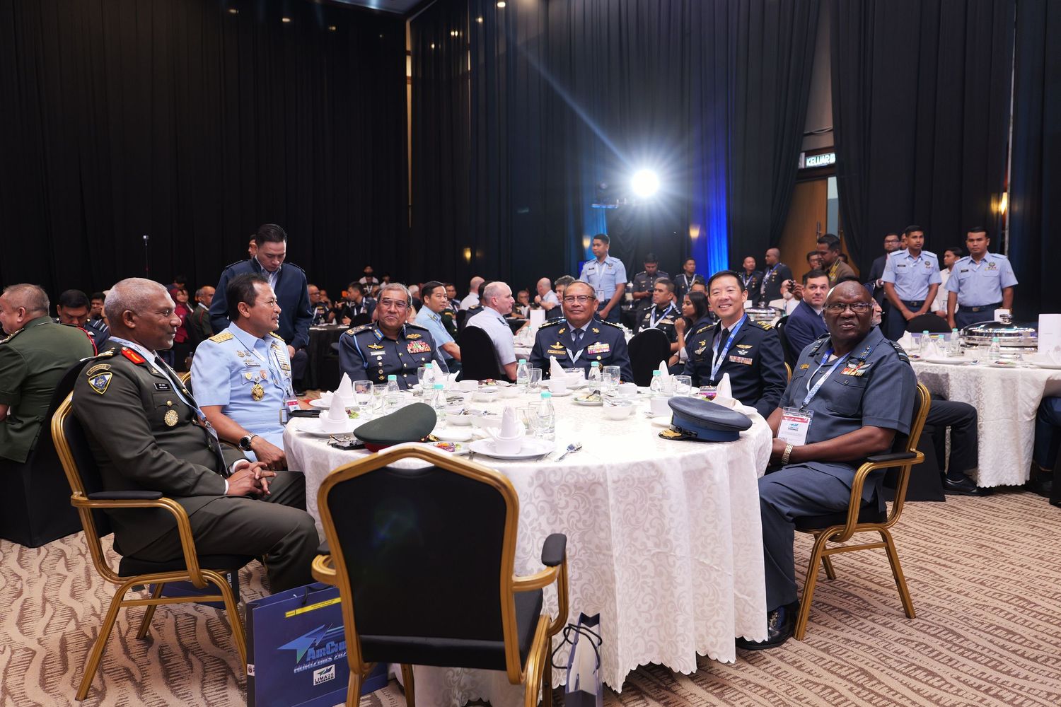 Conference attendees seated at round tables during a formal business gathering in a hotel ballroom.