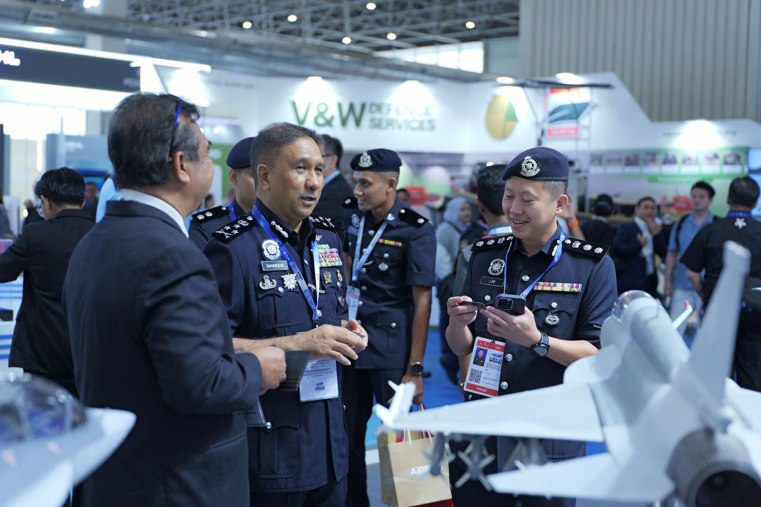 Officials and personnel inspecting equipment at technology exhibition with bright overhead lighting.