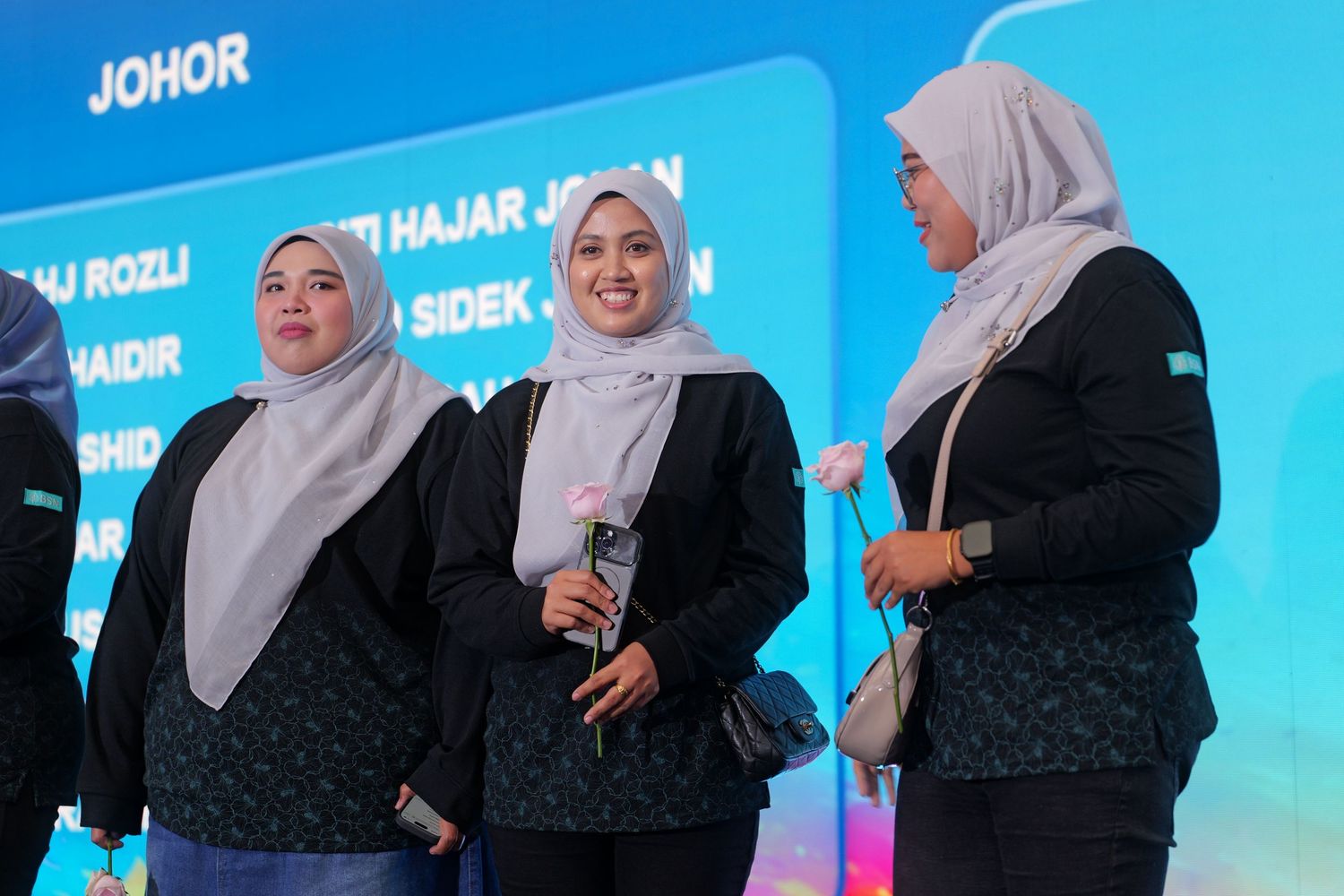 Three women in hijabs standing on stage at a Johor corporate presentation event.