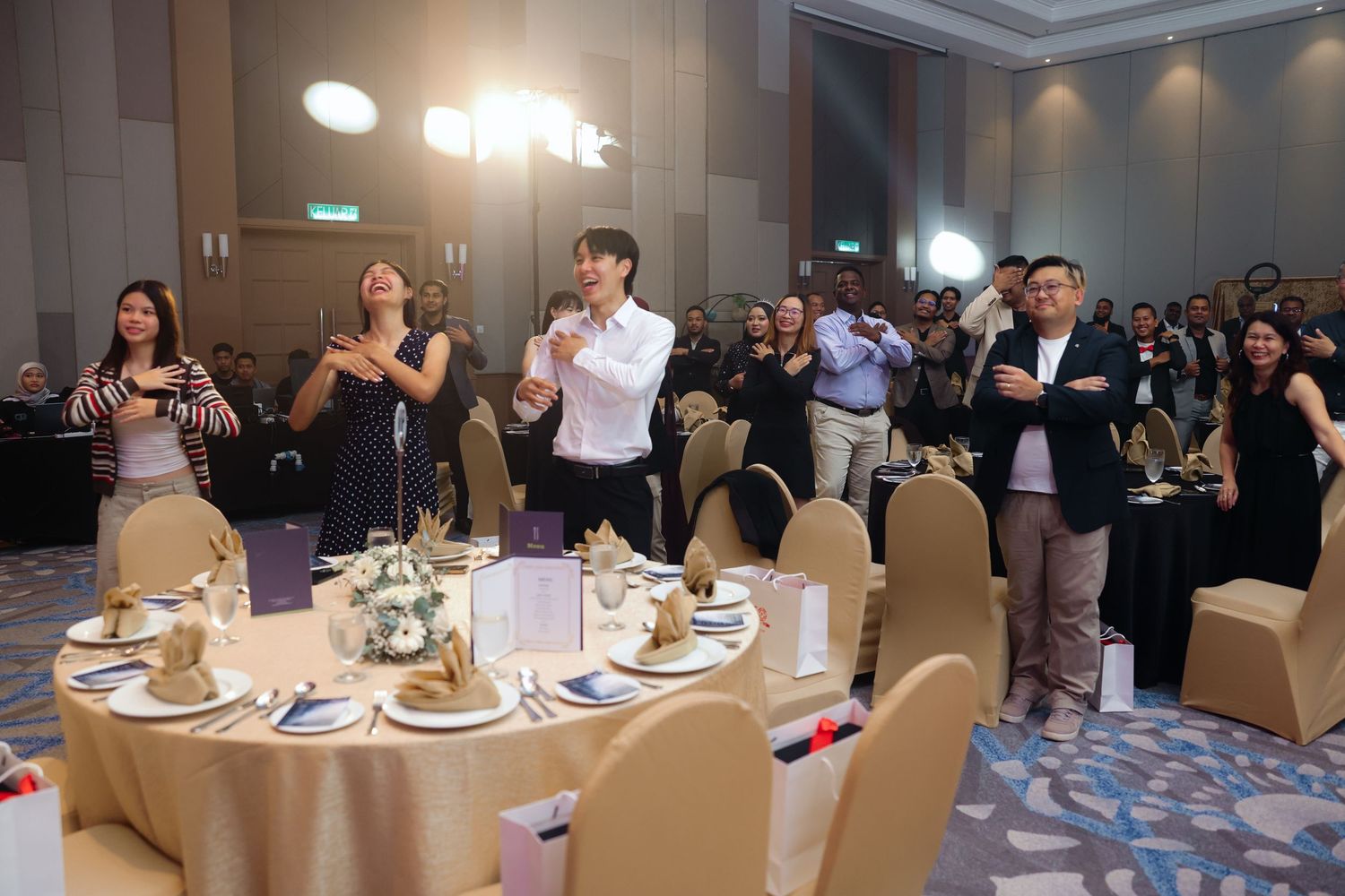 Guests celebrate and applaud at elegant banquet hall dinner event with round tables.