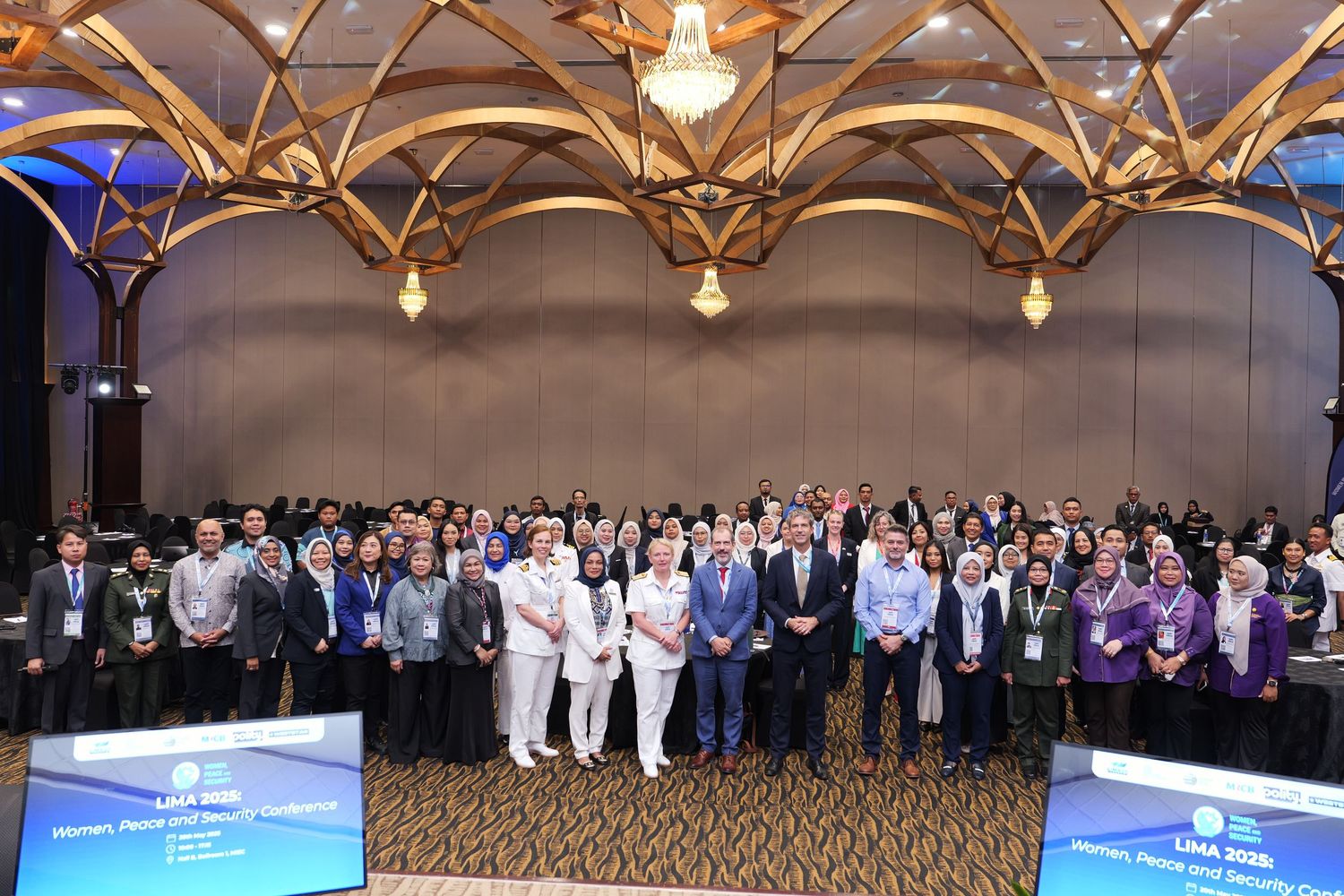 Large group photo of conference attendees standing together under ornate ceiling with chandelier.