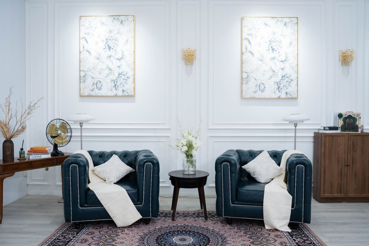 Elegant living room with two teal velvet armchairs, white throw pillows, and floral artwork on light gray walls.