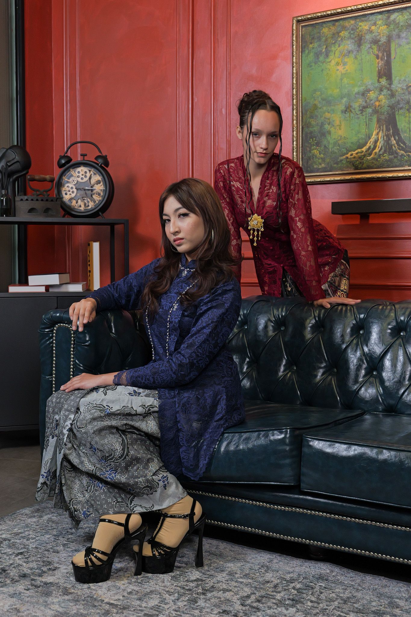 Person in navy blue outfit lounges on black leather couch with decorative red walls and artwork in background.