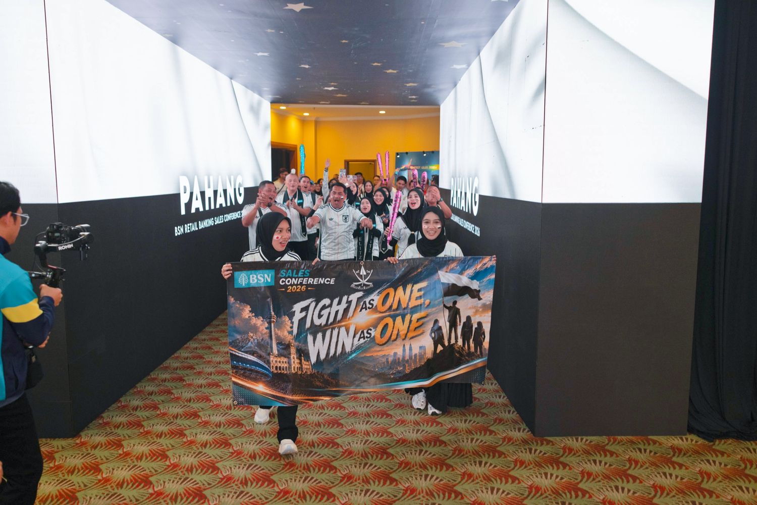 Group of people posing with a Fight as One Win as One banner at an esports gaming event in a decorated venue.