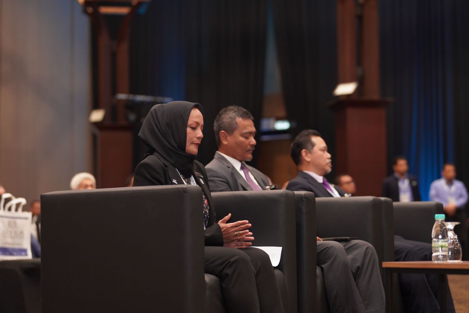 Business professionals seated at conference tables during formal meeting or presentation.