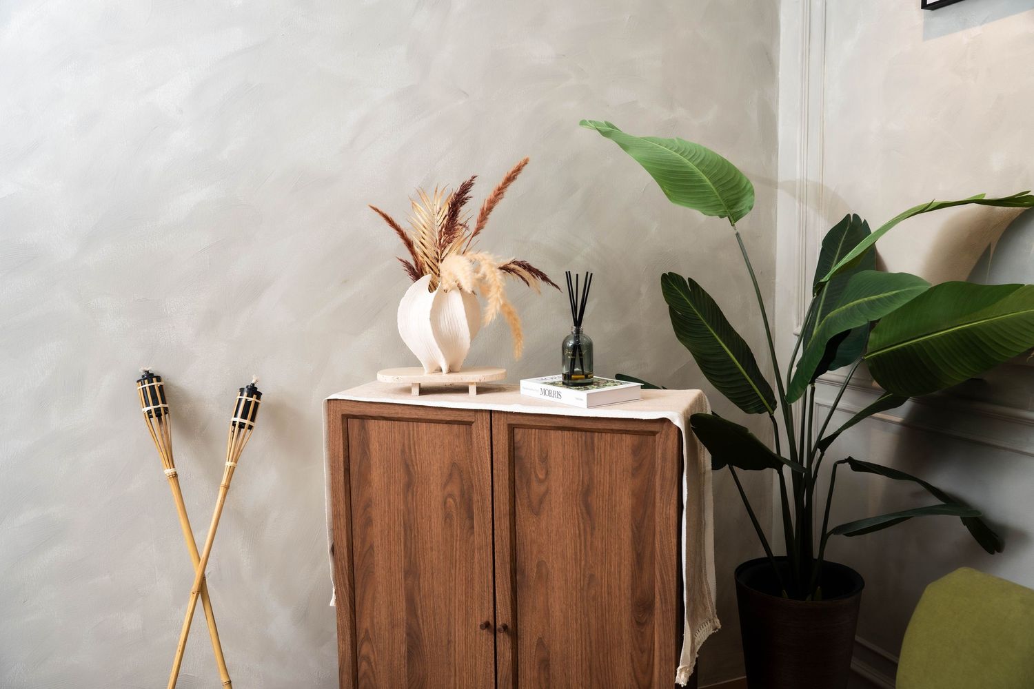 Wooden sideboard cabinet with decorative crossed arrows and potted plant against gray textured wall in modern interior.