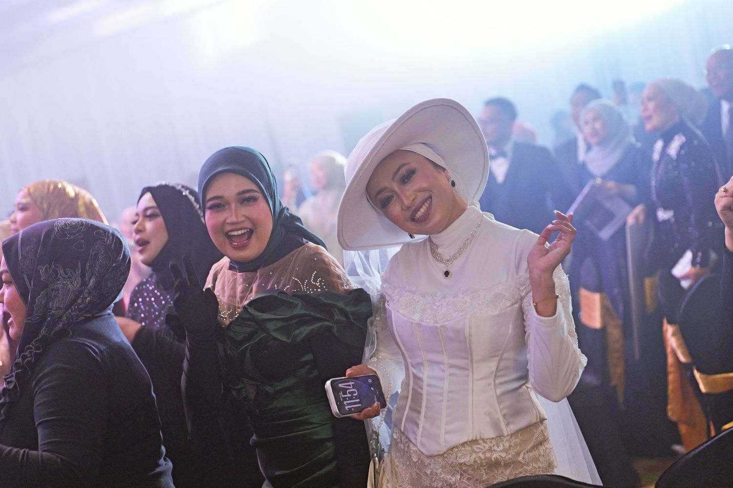 Two women smiling and posing together at a formal event, one wearing an elegant white hat.