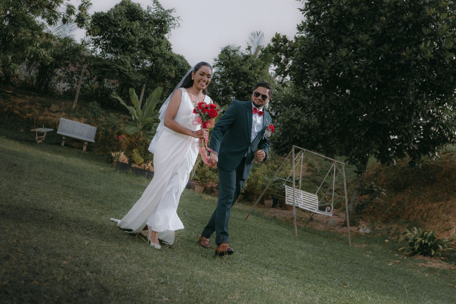 Wedding couple poses in outdoor garden setting with lush greenery in background.