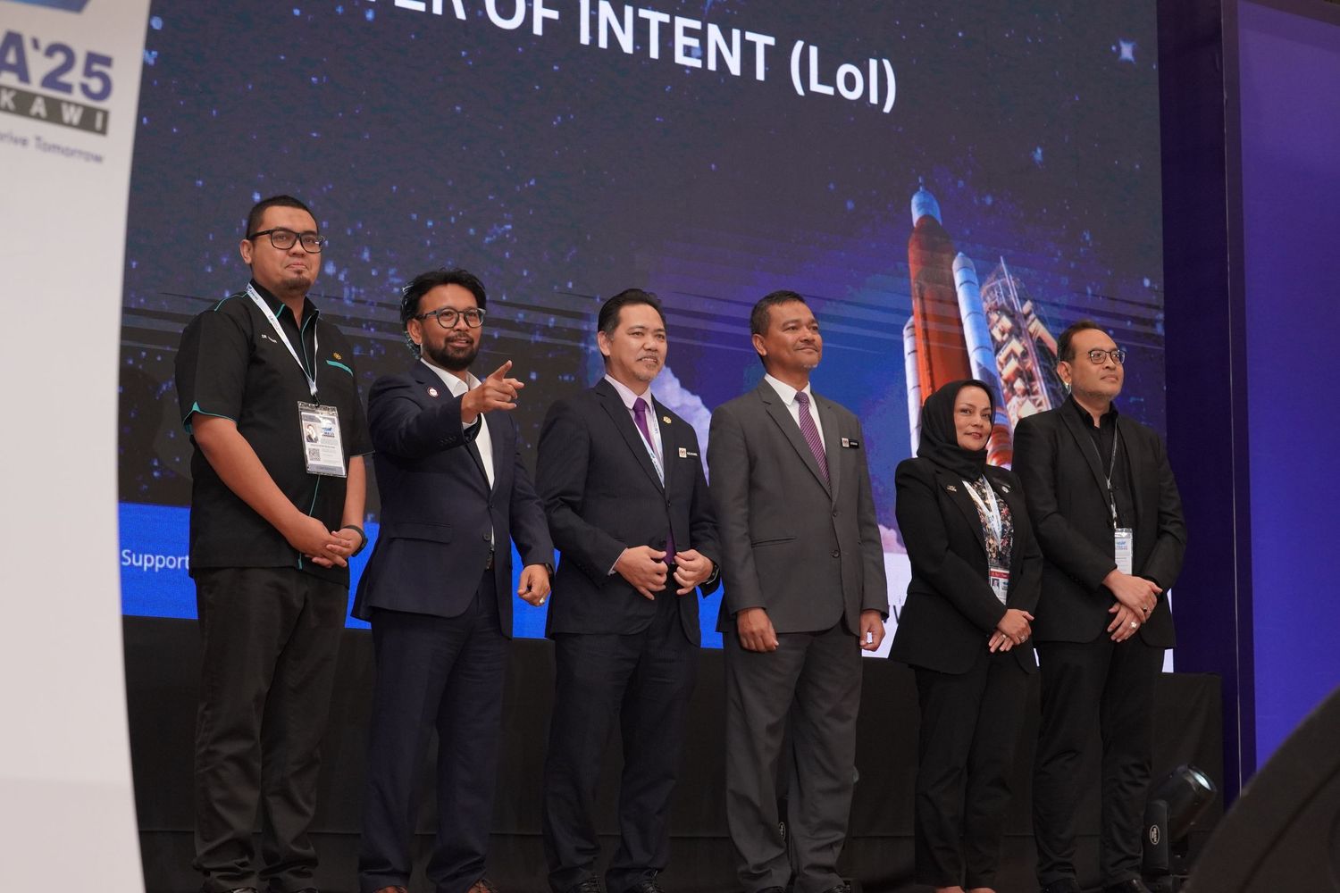Large group of executives standing on stage during corporate event with LED screens displaying text.
