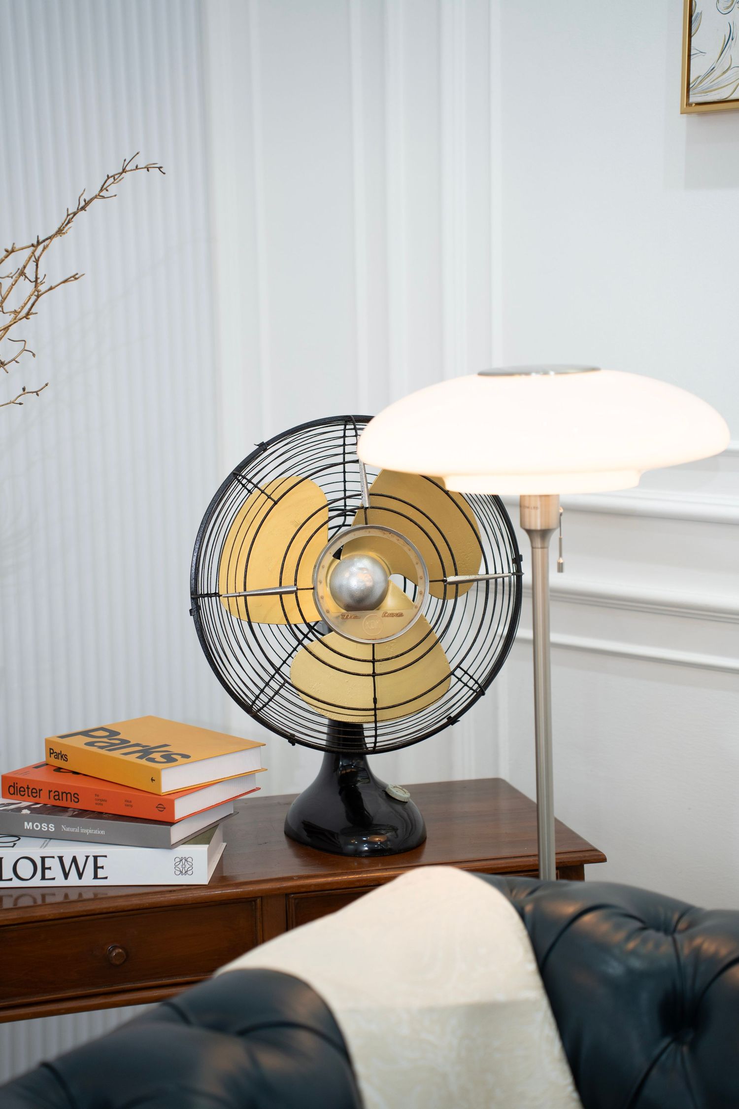 Vintage-style circular metal fan sculpture displayed on wooden furniture with books and modern decor elements.