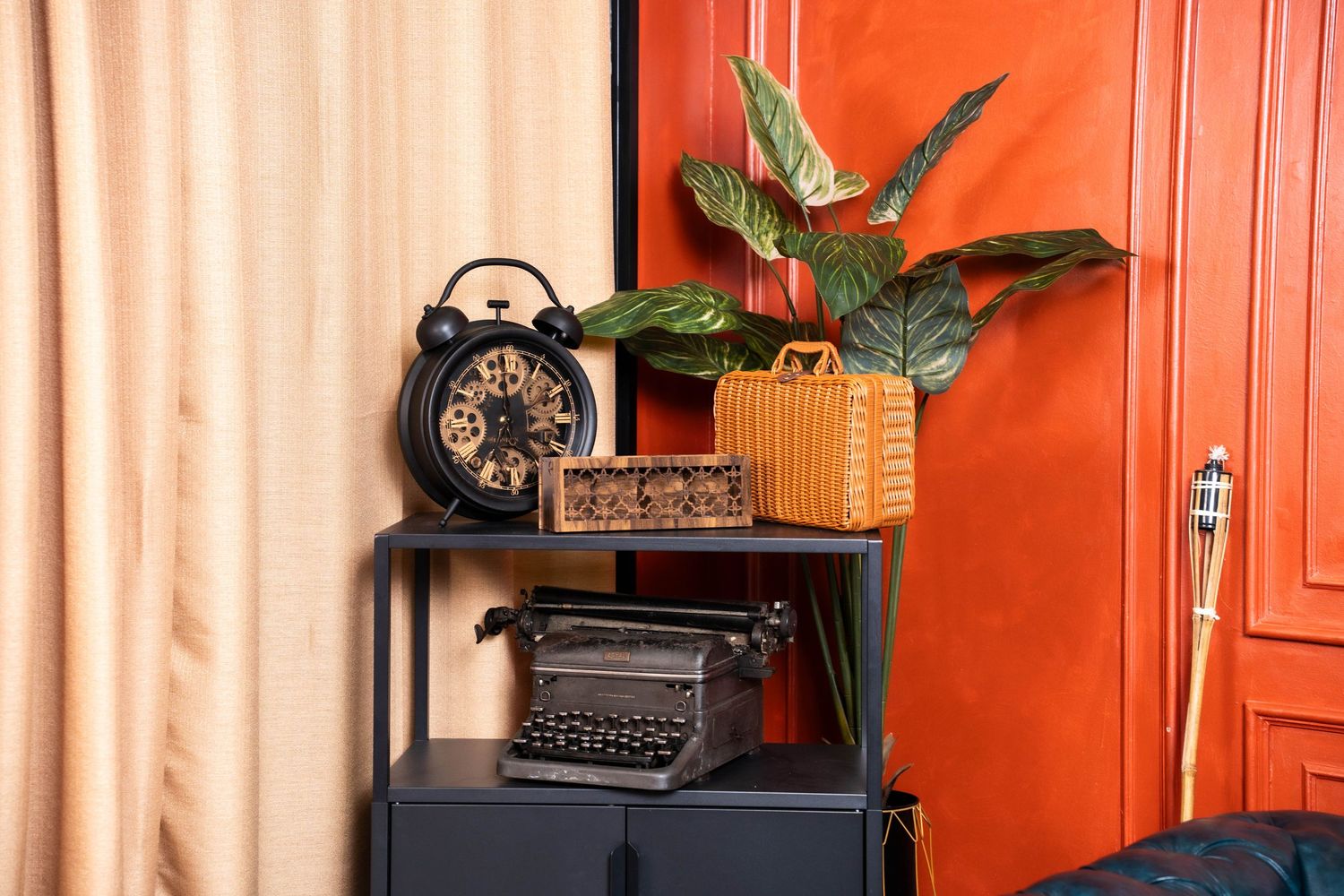 Vintage rotary telephone sits on wooden table against vibrant orange wall with decorative plants and curtains.