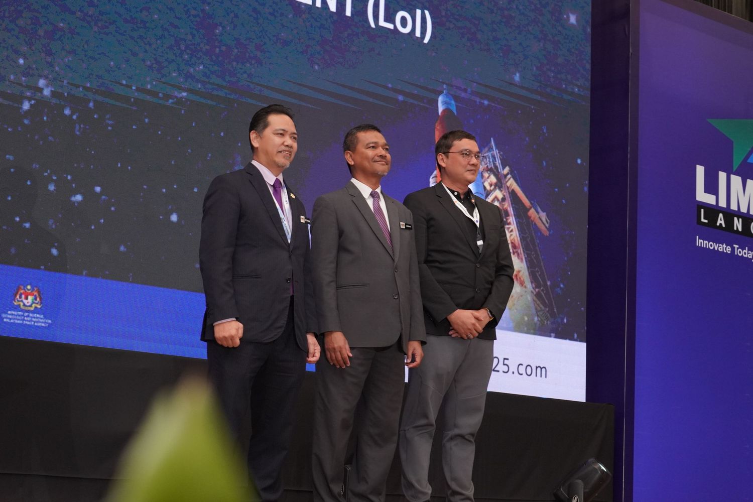 Business executives gathered on stage at LIMA corporate event with display screens in background.