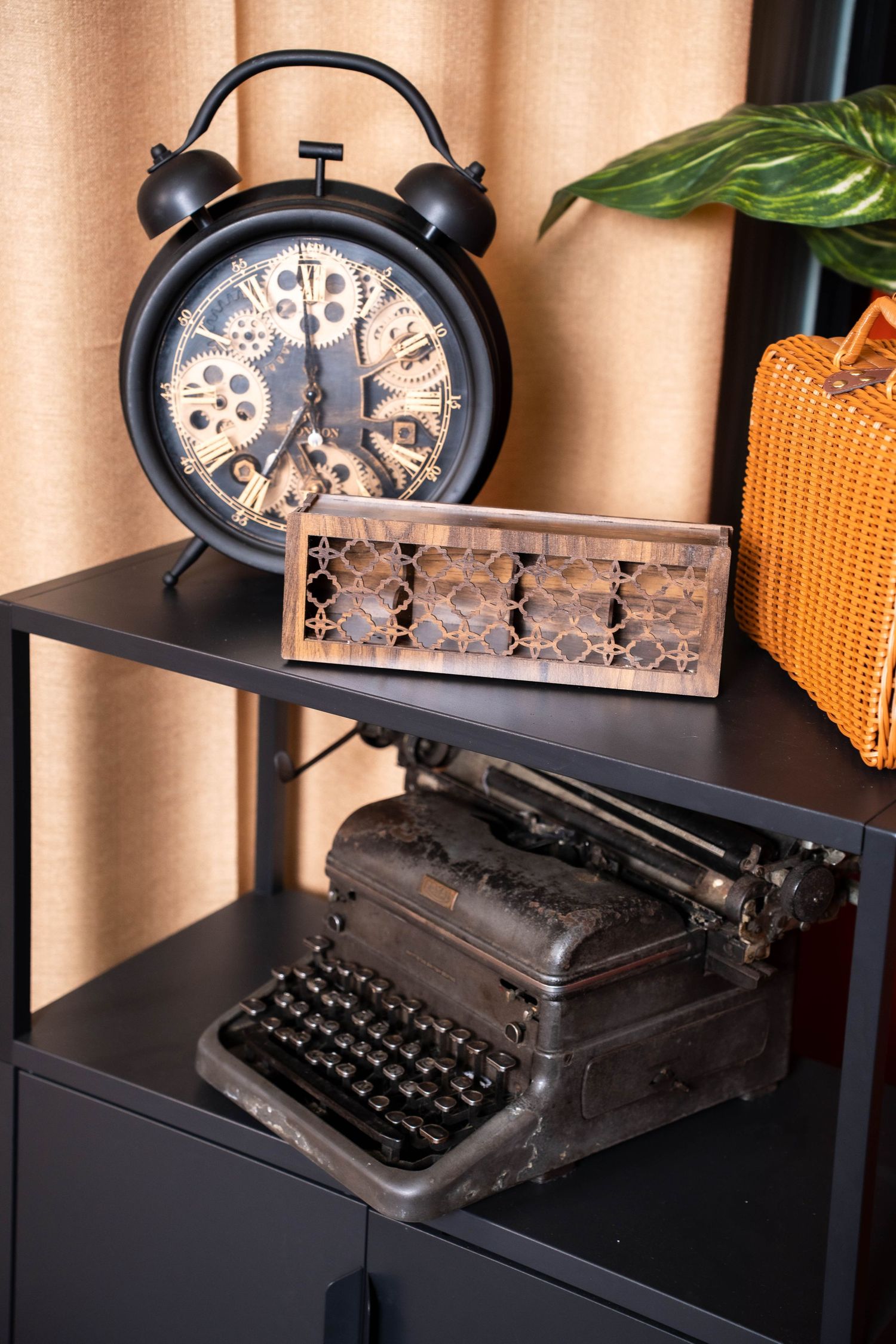 Vintage decor display with black alarm clock, wooden abacus, and antique typewriter on dark shelving unit.